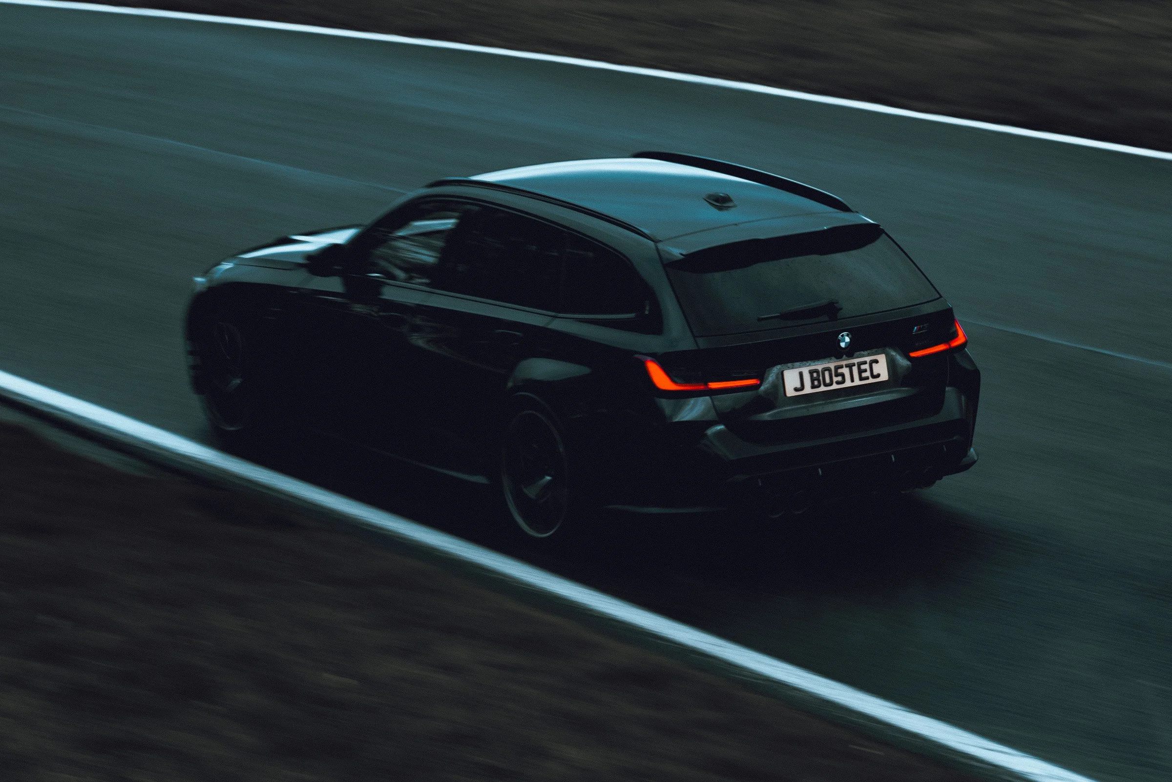 A black BMW car driving on a race track during the evening, with motion blur showing speed.