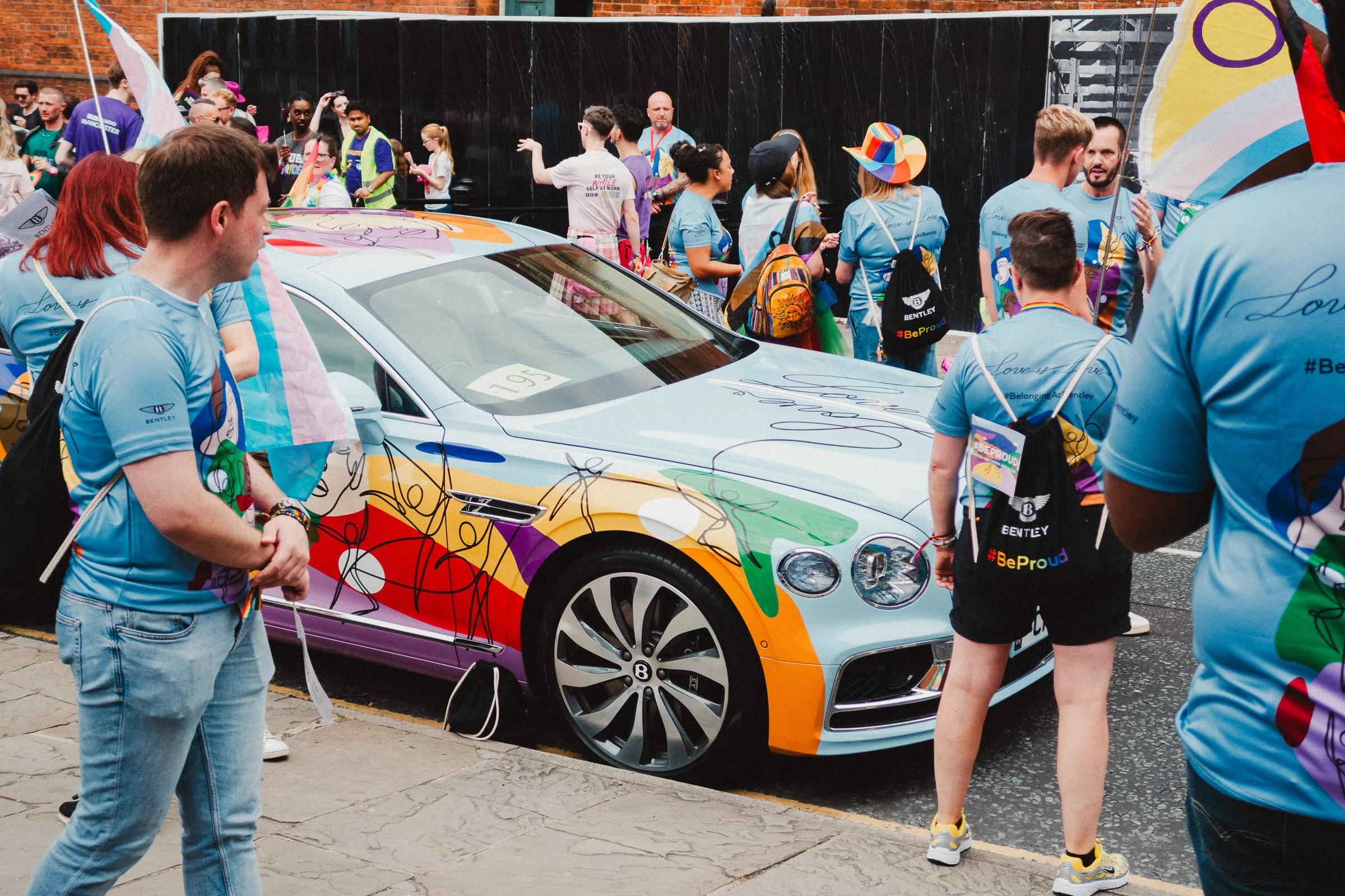 People participating at Manchester Pride parade surrounding a colourful Bentley car with rainbow designs.
