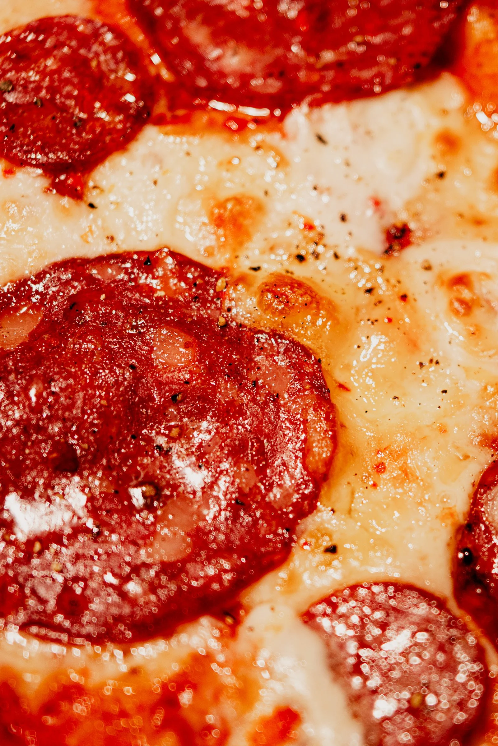 Close-up of a pepperoni pizza showing melted cheese, tomato sauce, and pepperoni slices seasoned with black pepper.