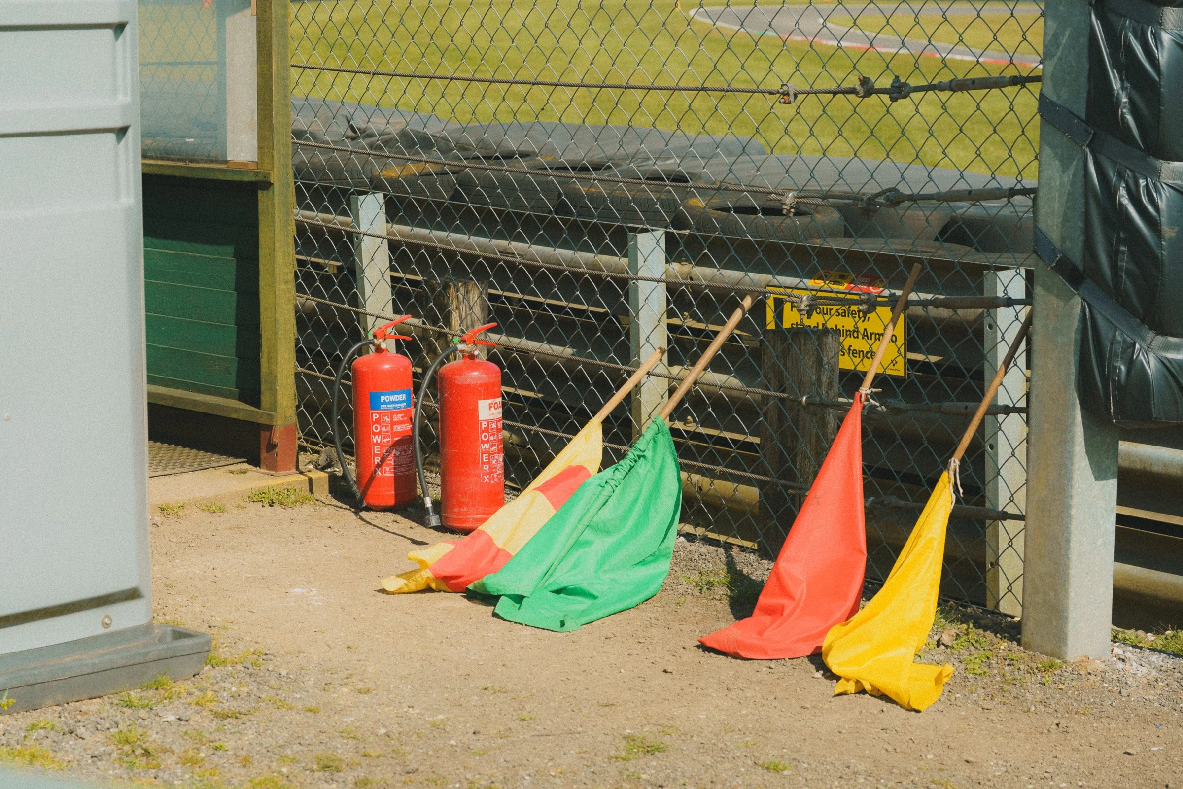 Fire extinguishers, a various track flags leaning against a chain-link fence at a marshal post at Cadwell Park, UK