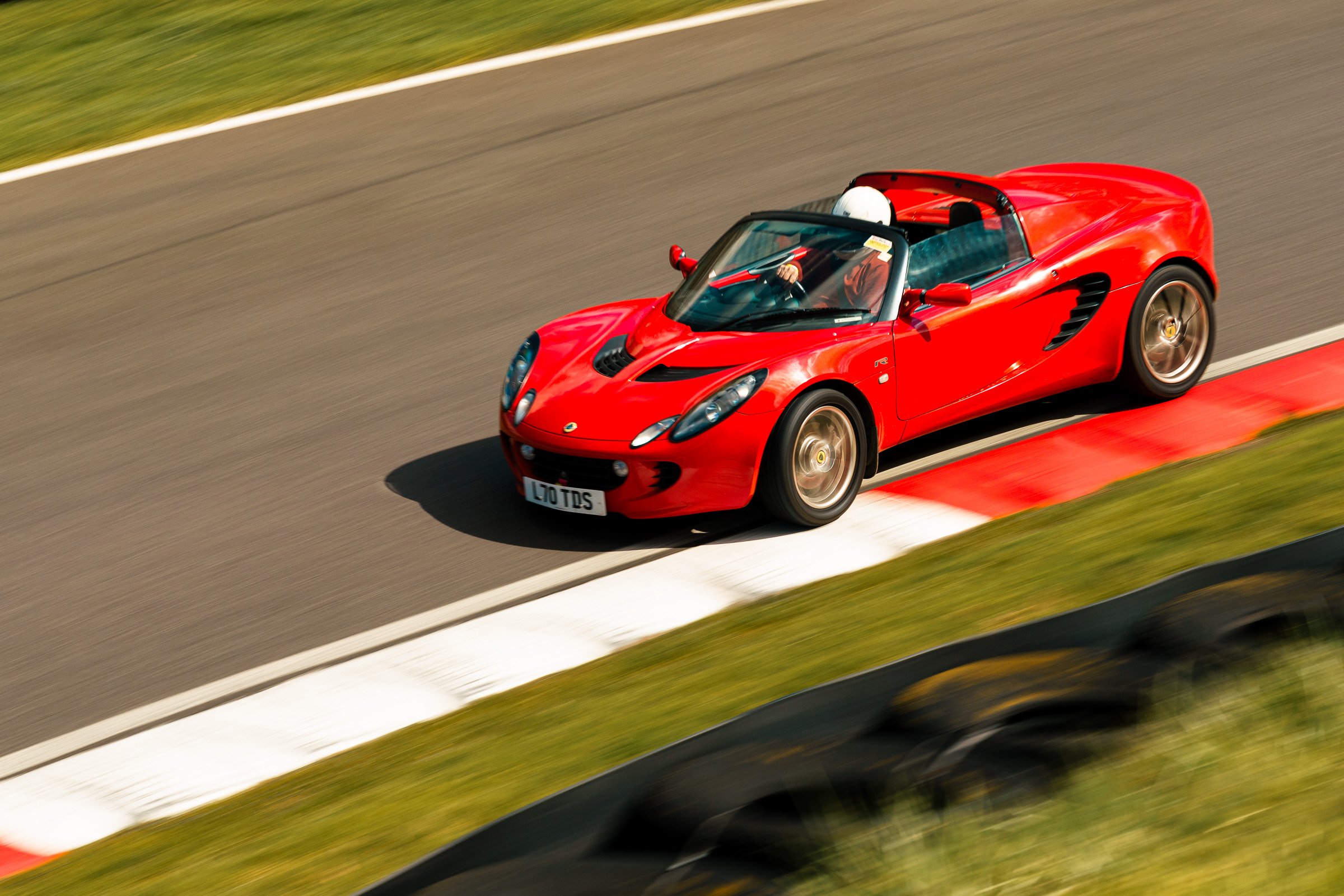 A red Lotus sports car on a racetrack, viewed from above as it takes a turn.
