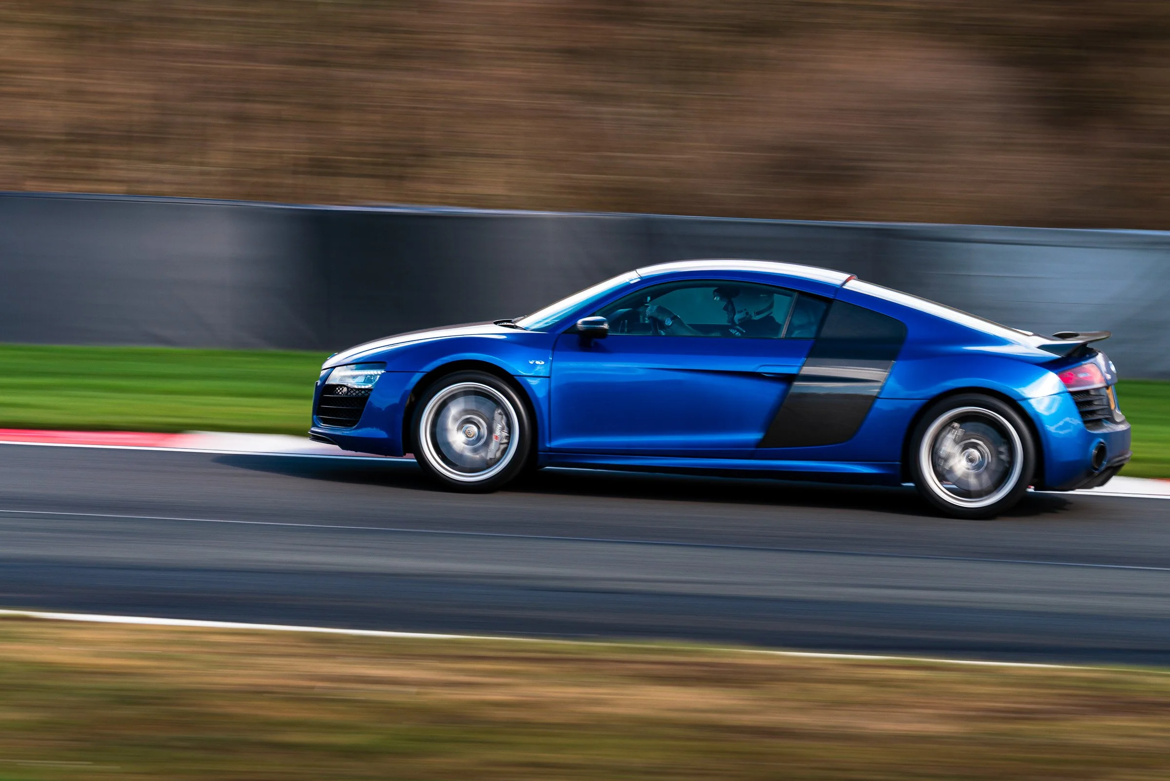 A blue sports car moving at high speed on a race track with a blurred background.