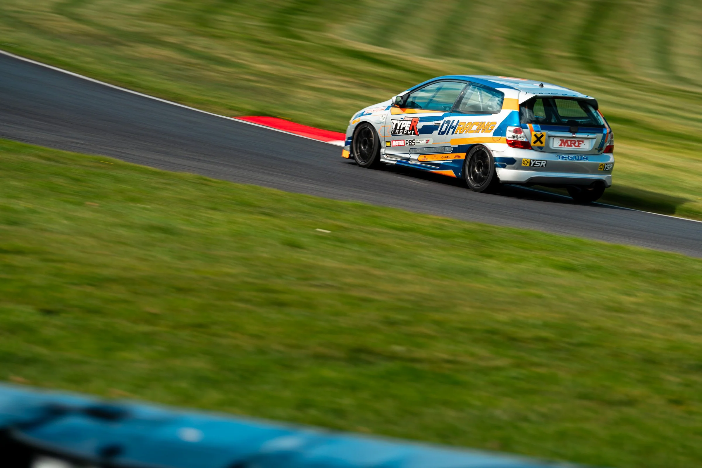 A race car on a racetrack with a blurred grassy background.