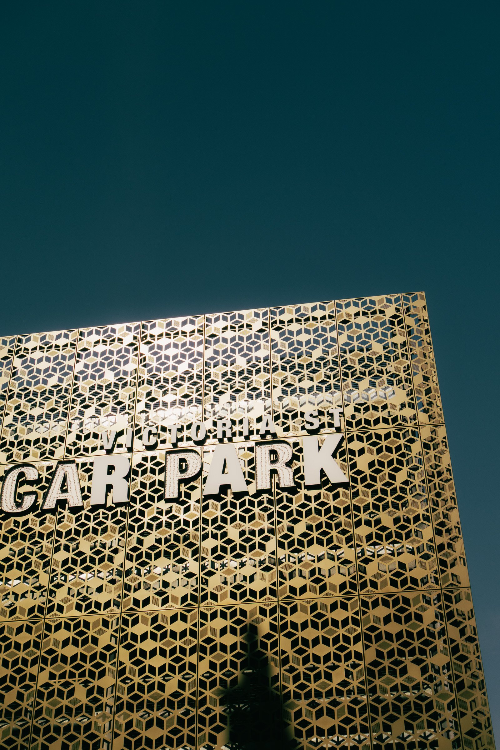 Close-up view of a building in Liverpool with a decorative golden honeycomb pattern and a sign that reads "Victoria St Car Park" and clear blue sky.