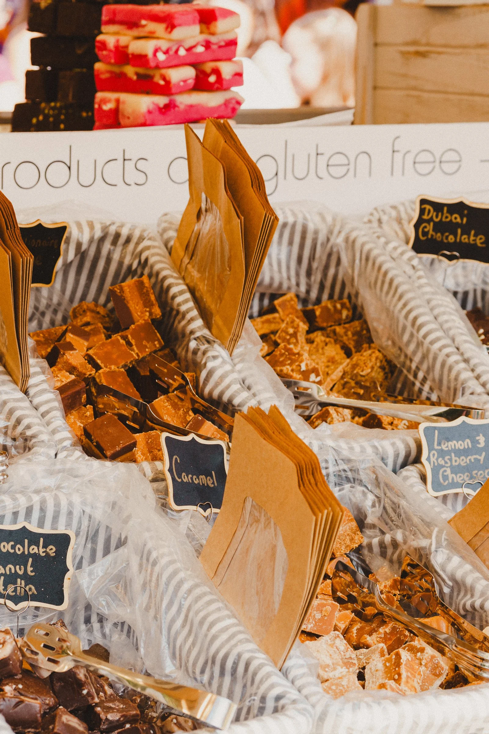 Display of various types of sweet treats in a market stall, with labels including caramel, lemon, and raspberry cheesecake.