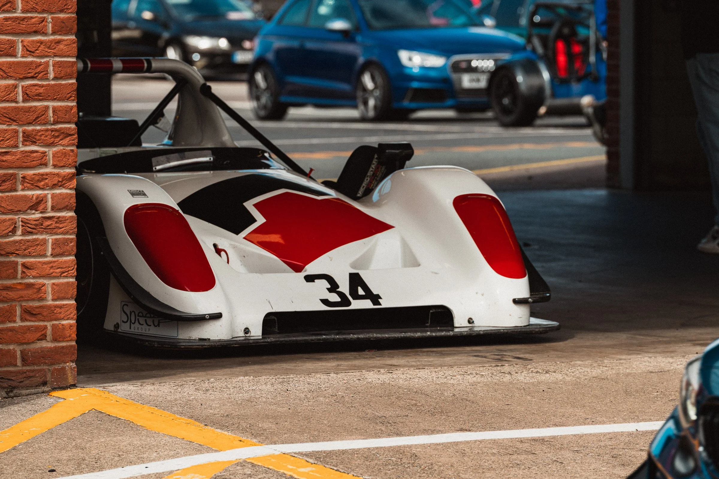 A white race car with red and black accents, numbered 34, parked in the paddock at Oulton Park circuit.
