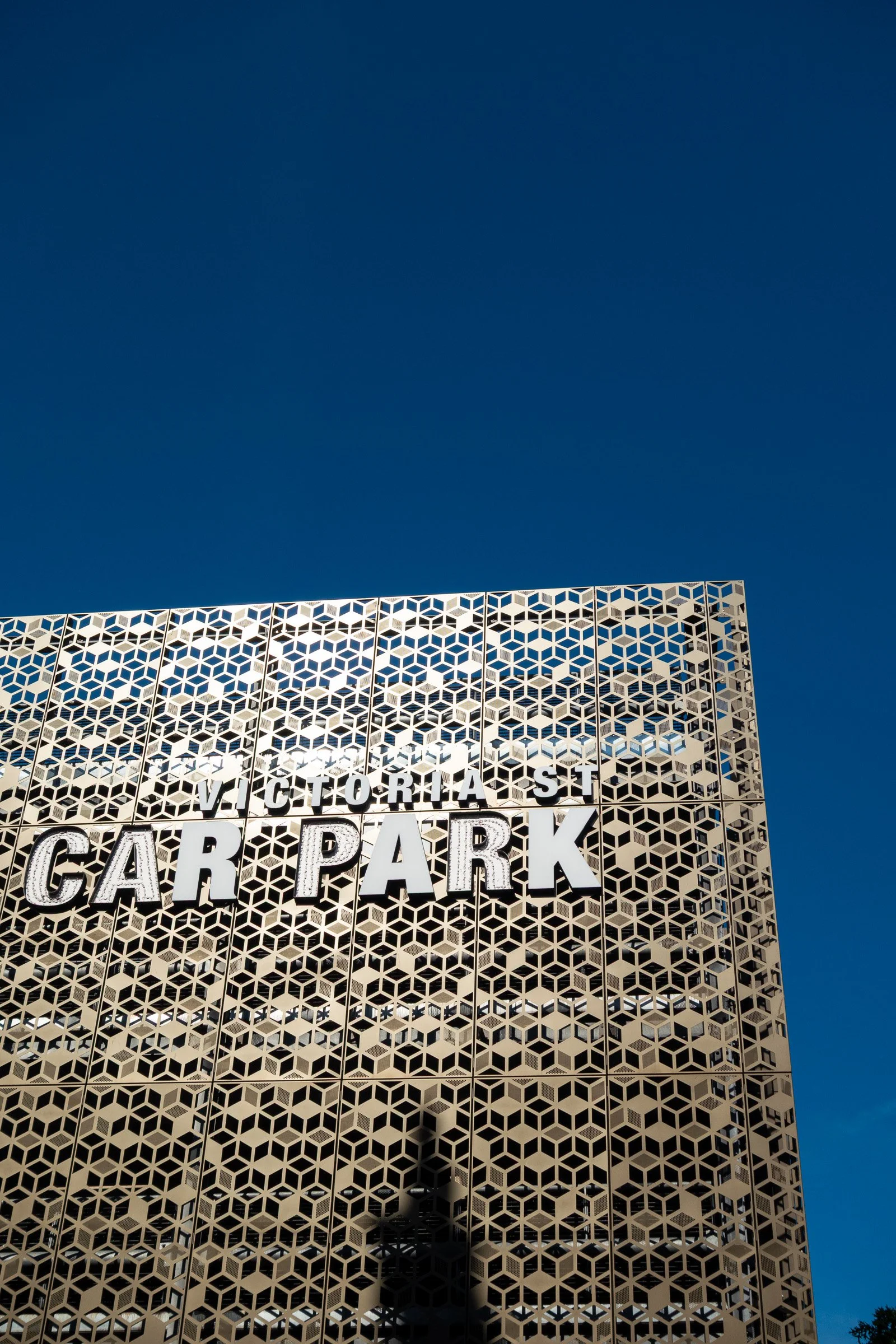 A tall building with a geometric patterned facade and large block letters spelling 'VICTORIA PARK' against a clear blue sky.