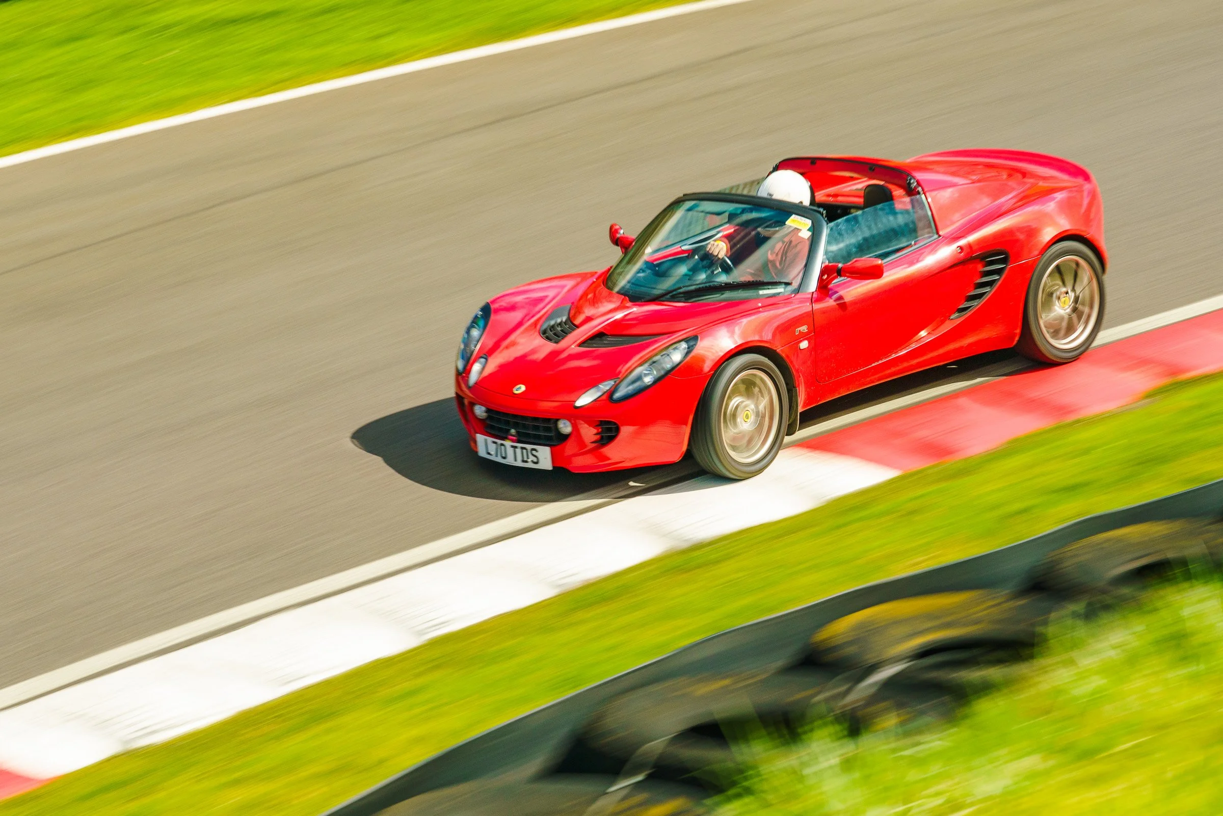 A red convertible sports car driving on a race track during the daytime.