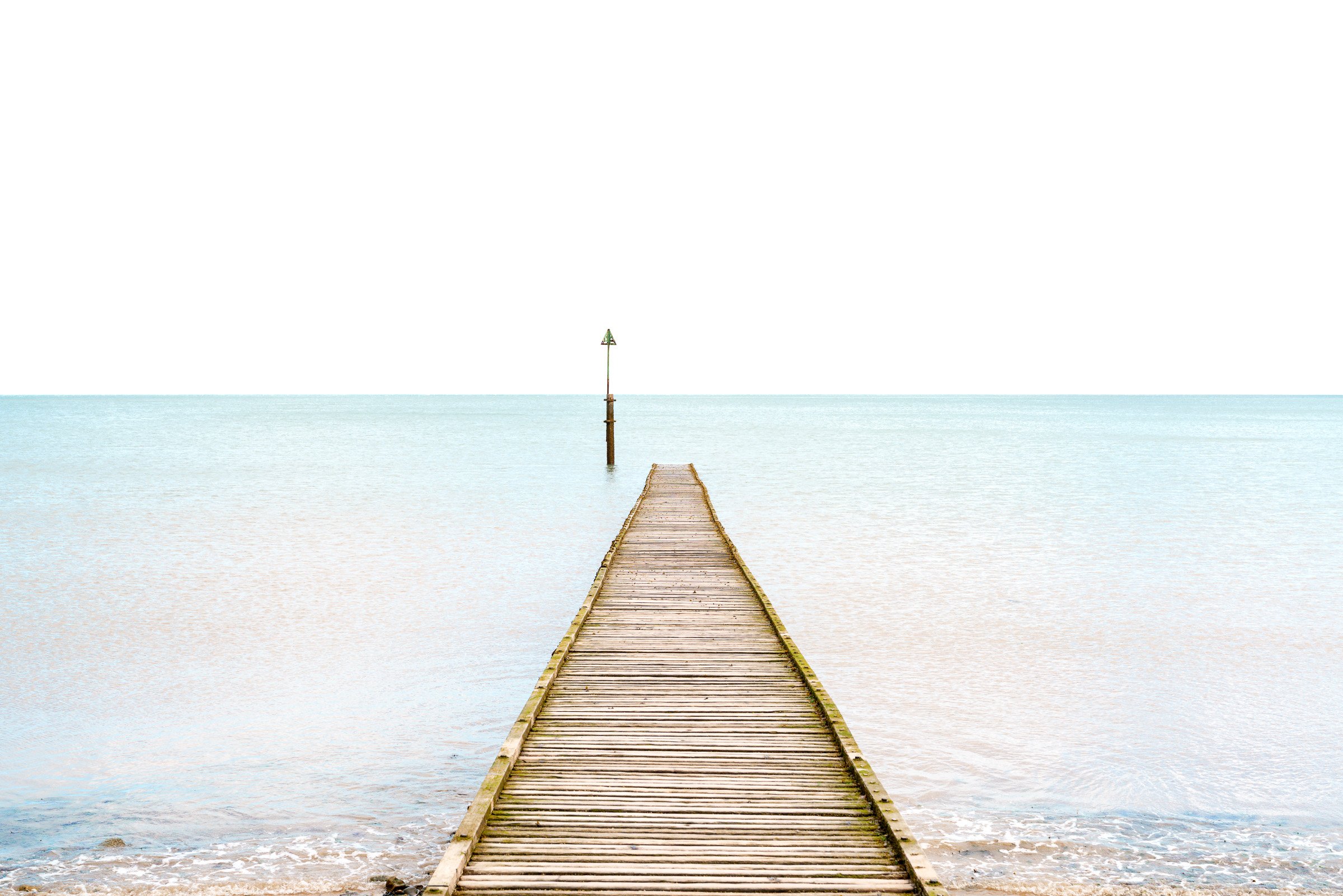 A wooden pier extends into calm ocean water with a green navigation marker at the end, under a clear sky.