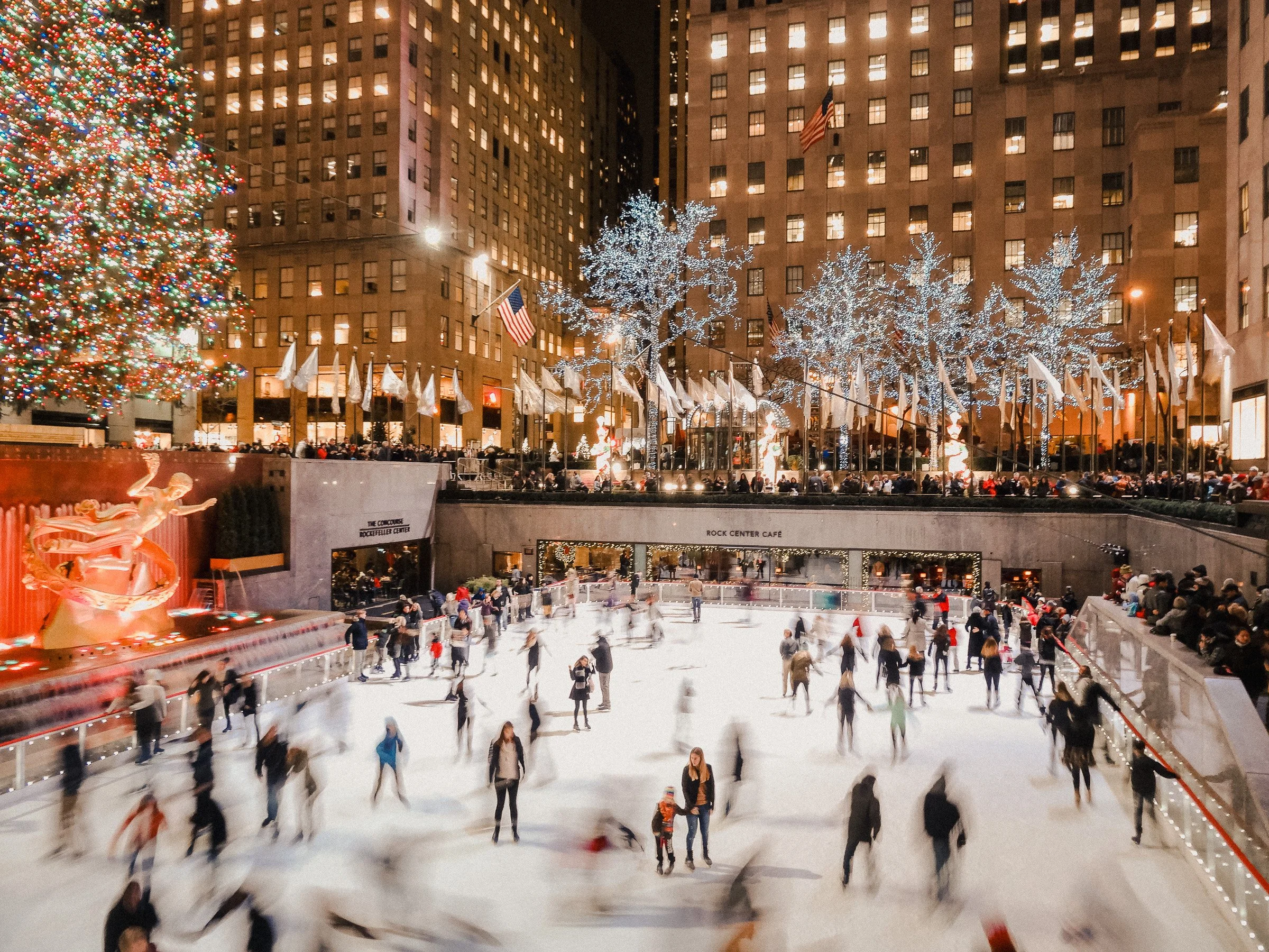 People ice skating at Rockefeller Center during Christmas time, decorated with a large Christmas tree and holiday lights.