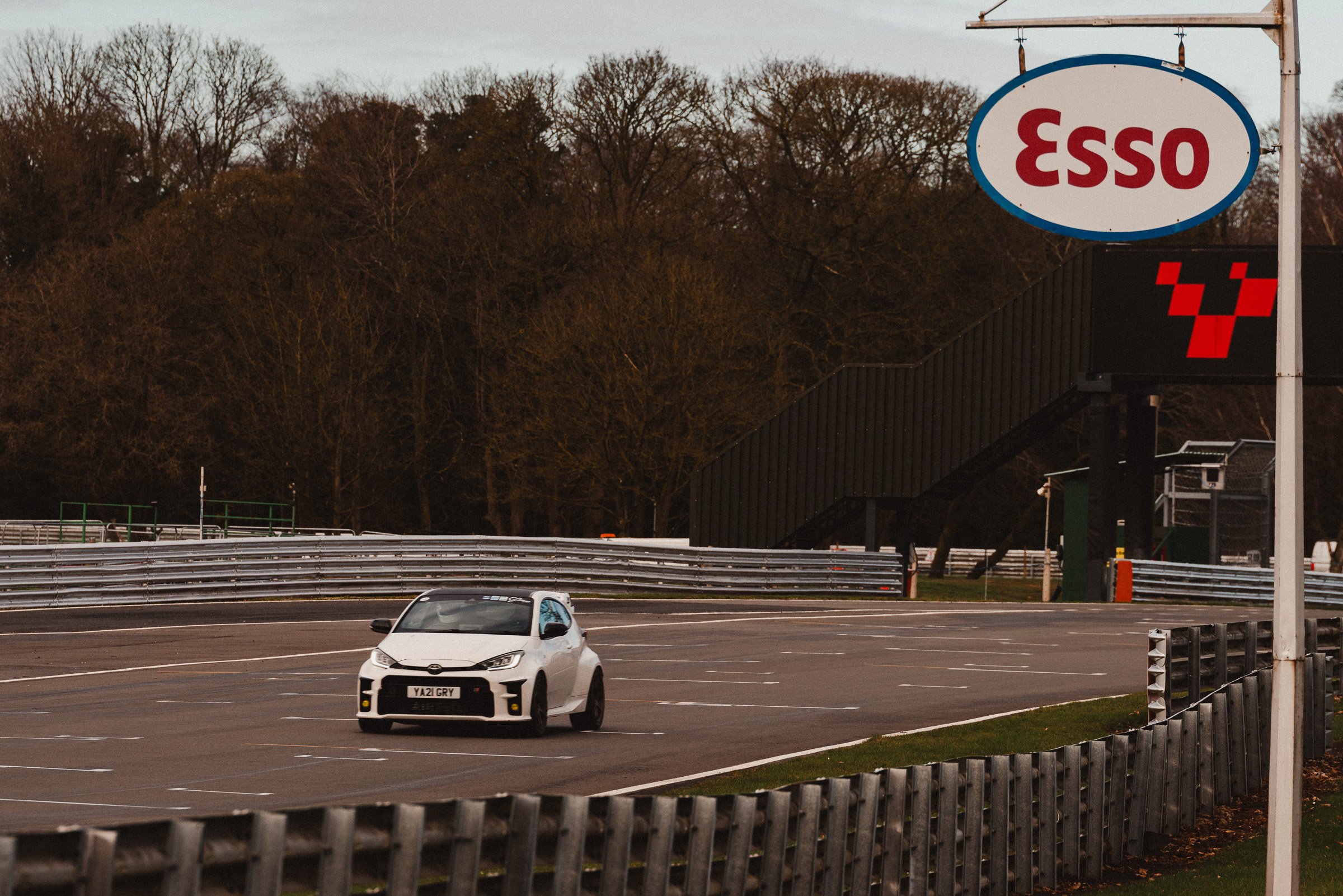 A white sports car at Oulton Park with a sign that reads 'ESSO' .