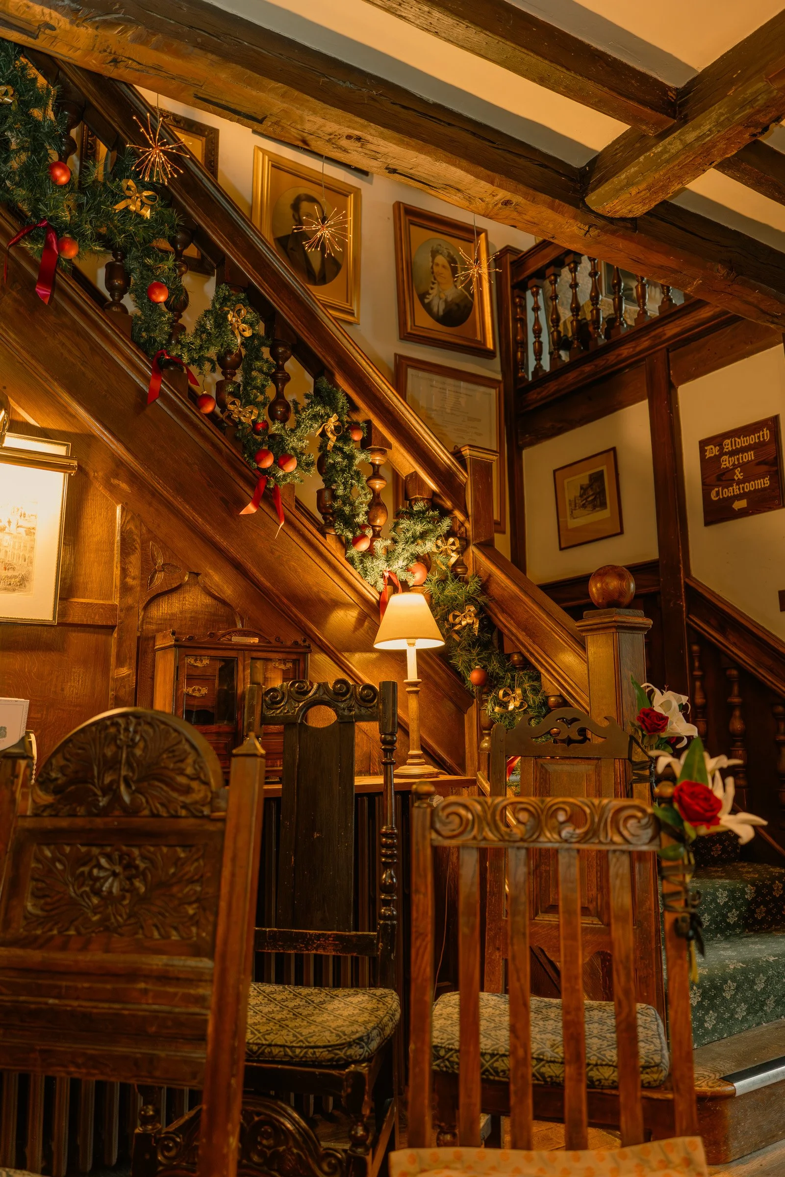 Decorated stairway in a cozy, vintage-style room with Christmas garland, framed portraits, and warm lighting.