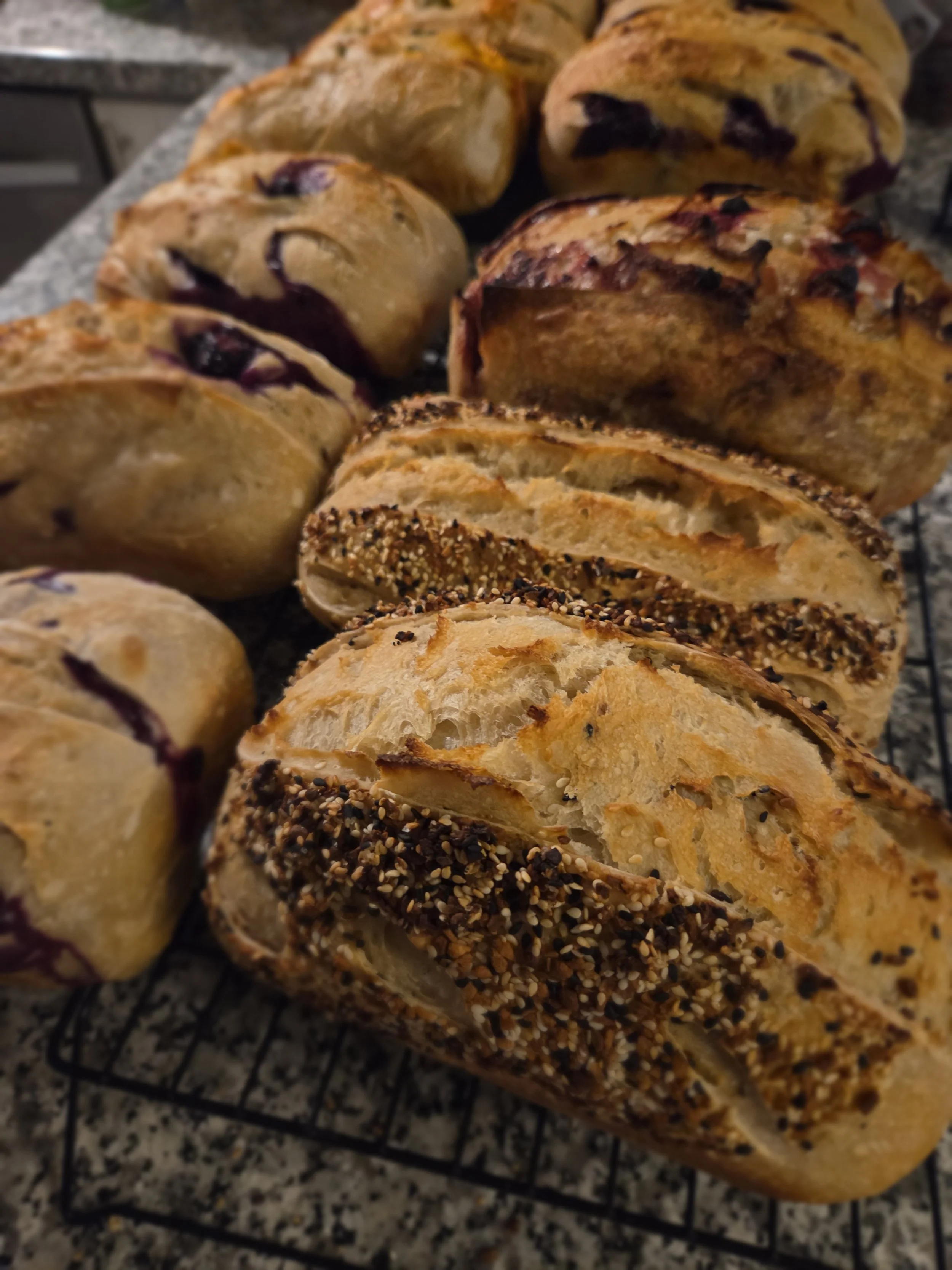 Assorted sourdough bread loaves, including blueberry, multigrain, and sesame seed-topped varieties.