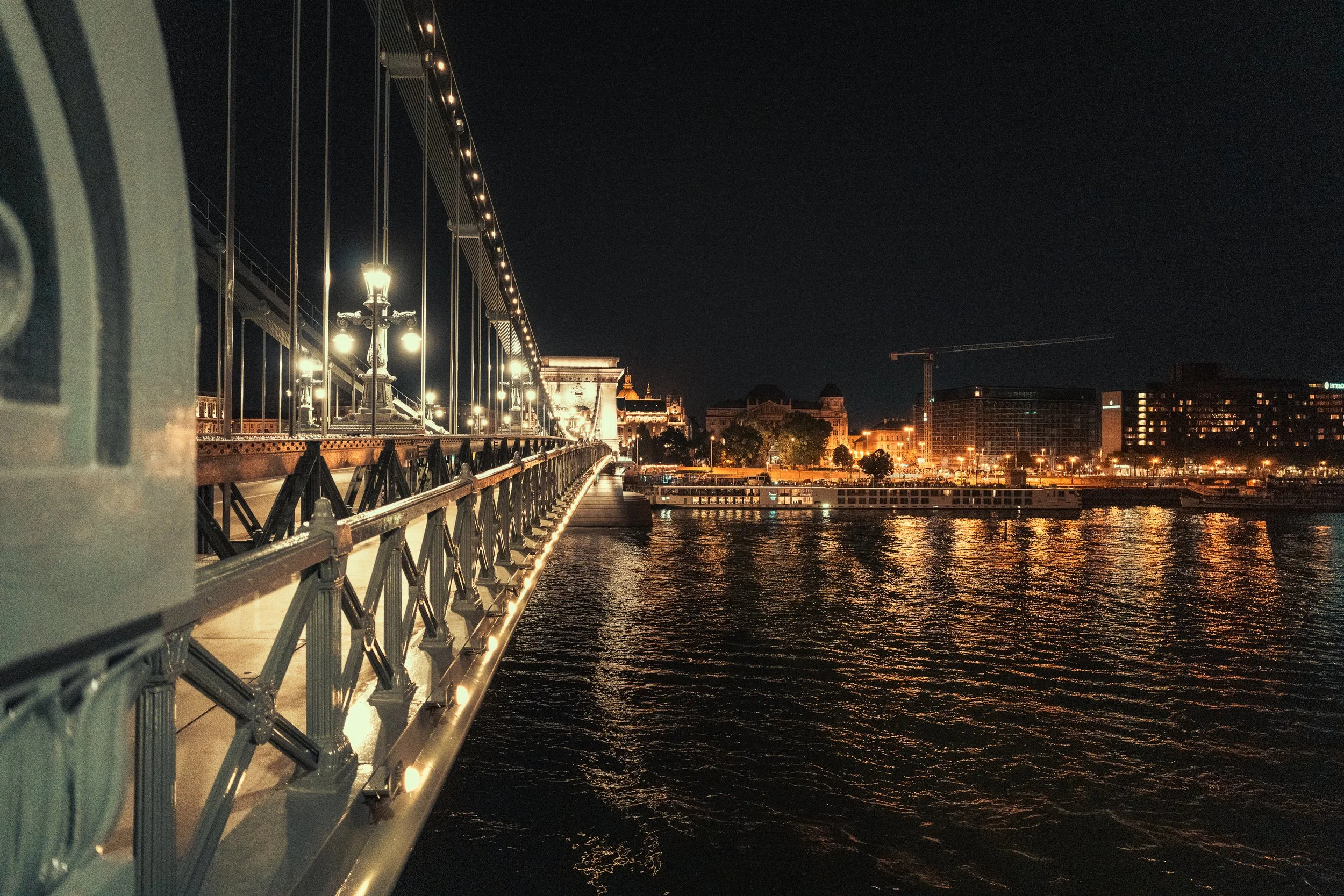 Night settles over the Danube, tracing light across the bridge and the calm river below.