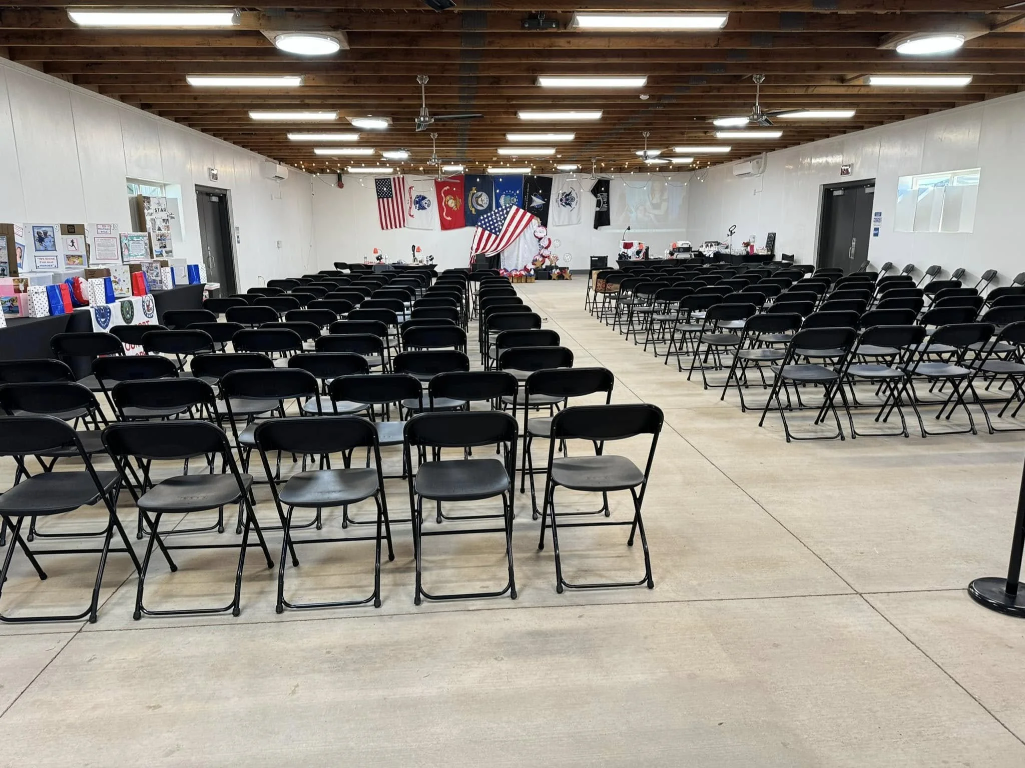 An indoor event space decorated with American flags and patriotic decorations, featuring rows of black folding chairs facing a stage in the background.
