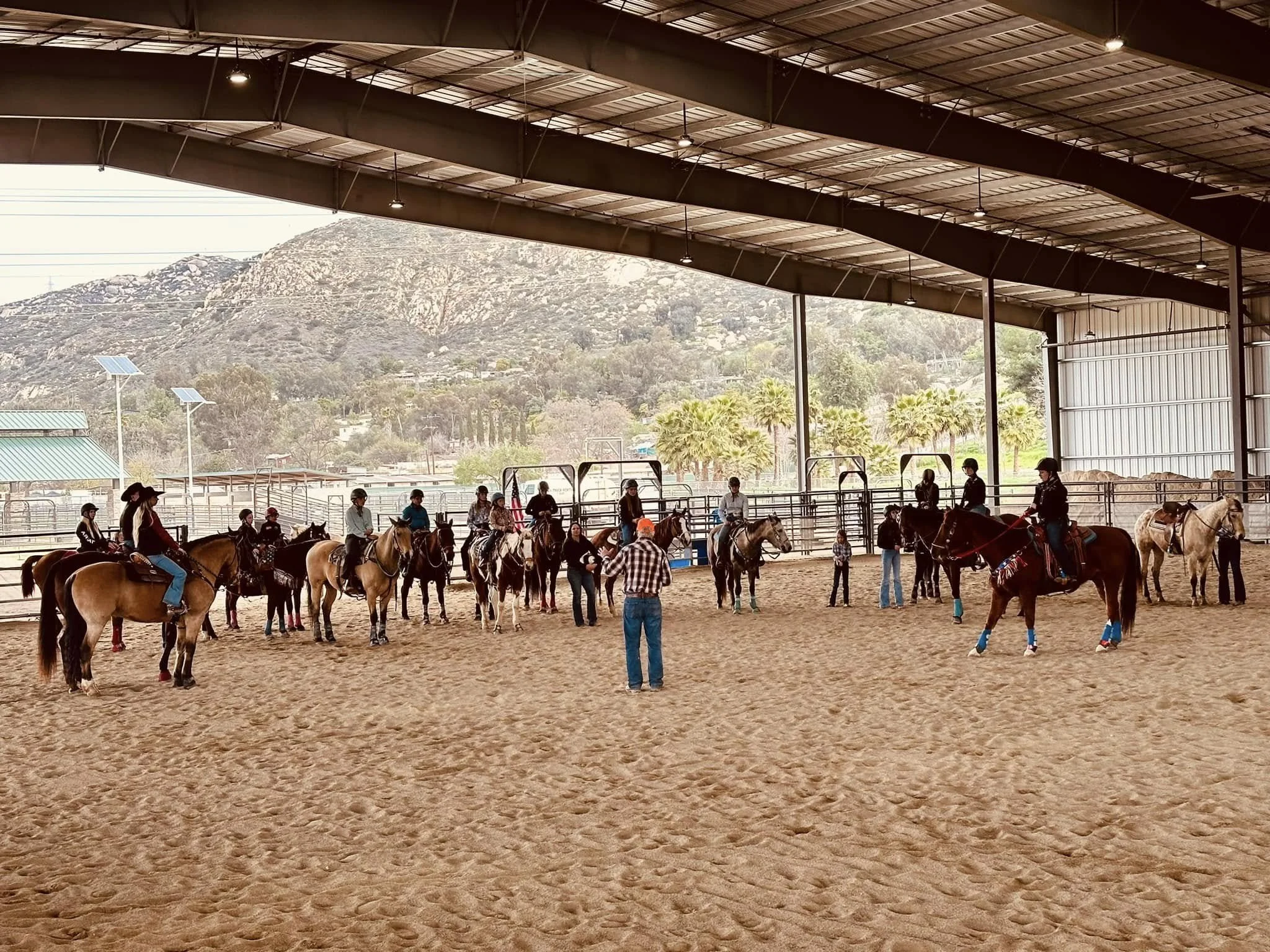 People riding horses inside an indoor riding arena with a mountainous landscape outside.
