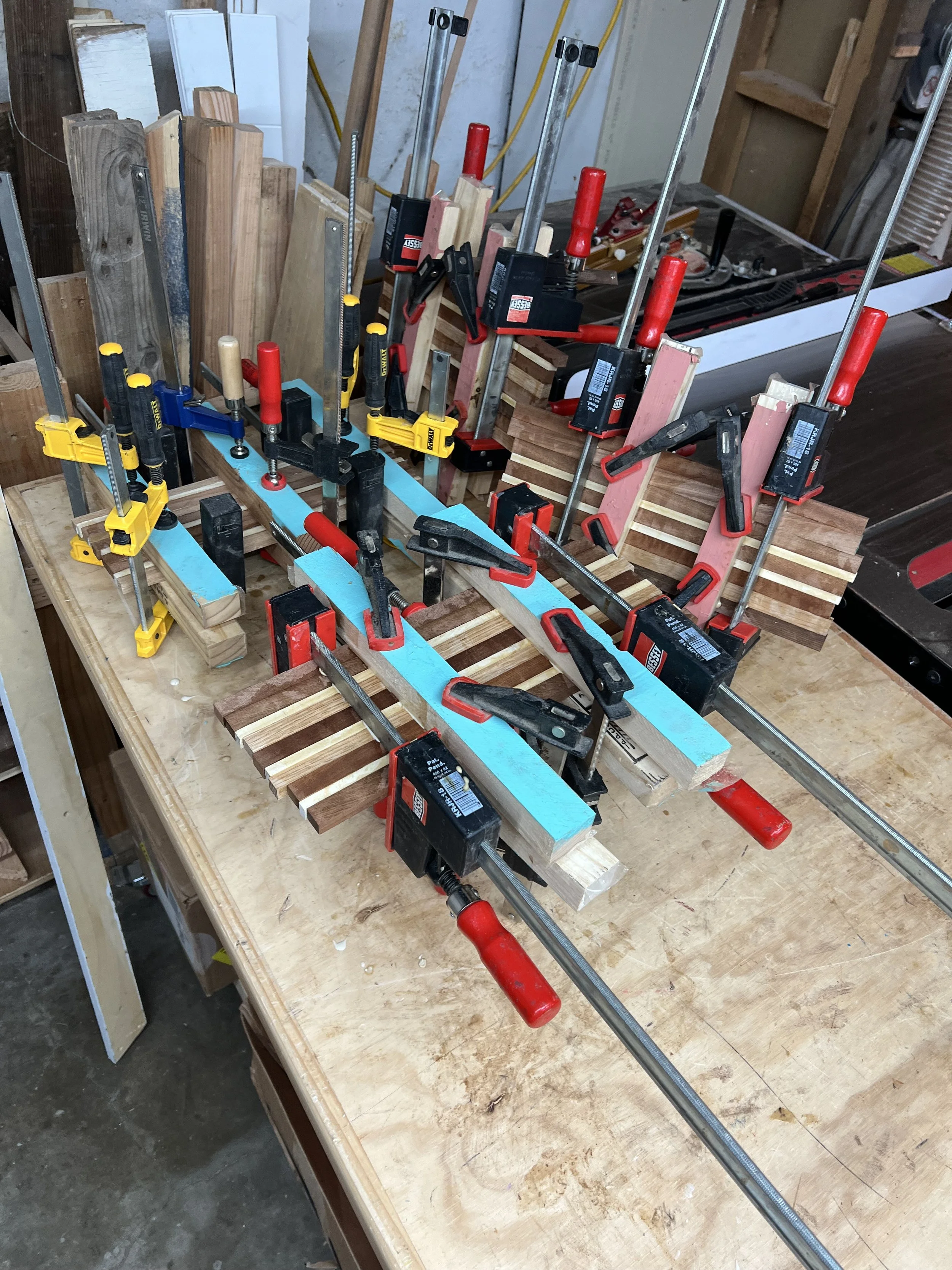 A woodworking workbench with clamps, pieces of wood, and tools in a workshop.