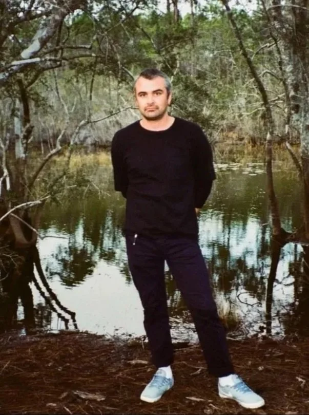 Cody Ross Rex, a musician and poet from Brooklyn, New York, stands in front of a cool natural background