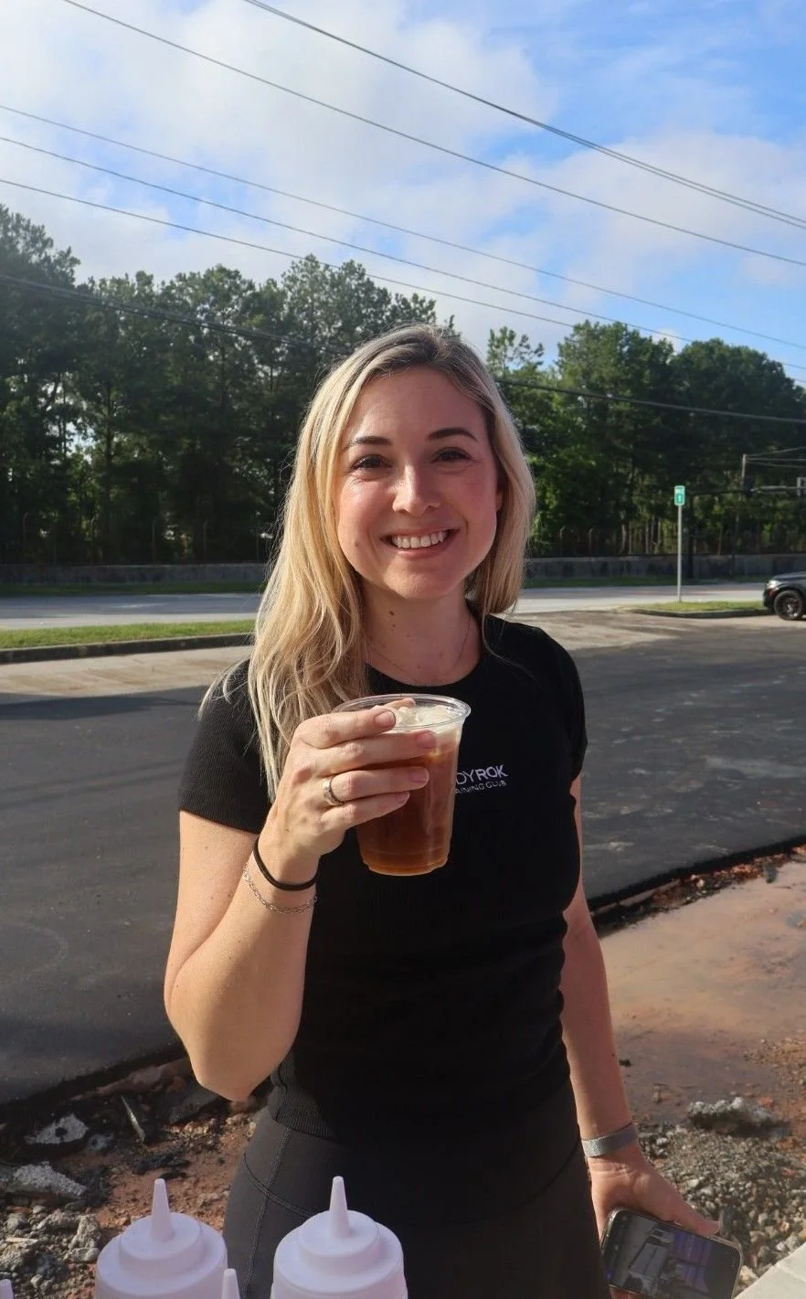 Woman posing with iced coffee cup outside Brookhaven Pilates studio opening