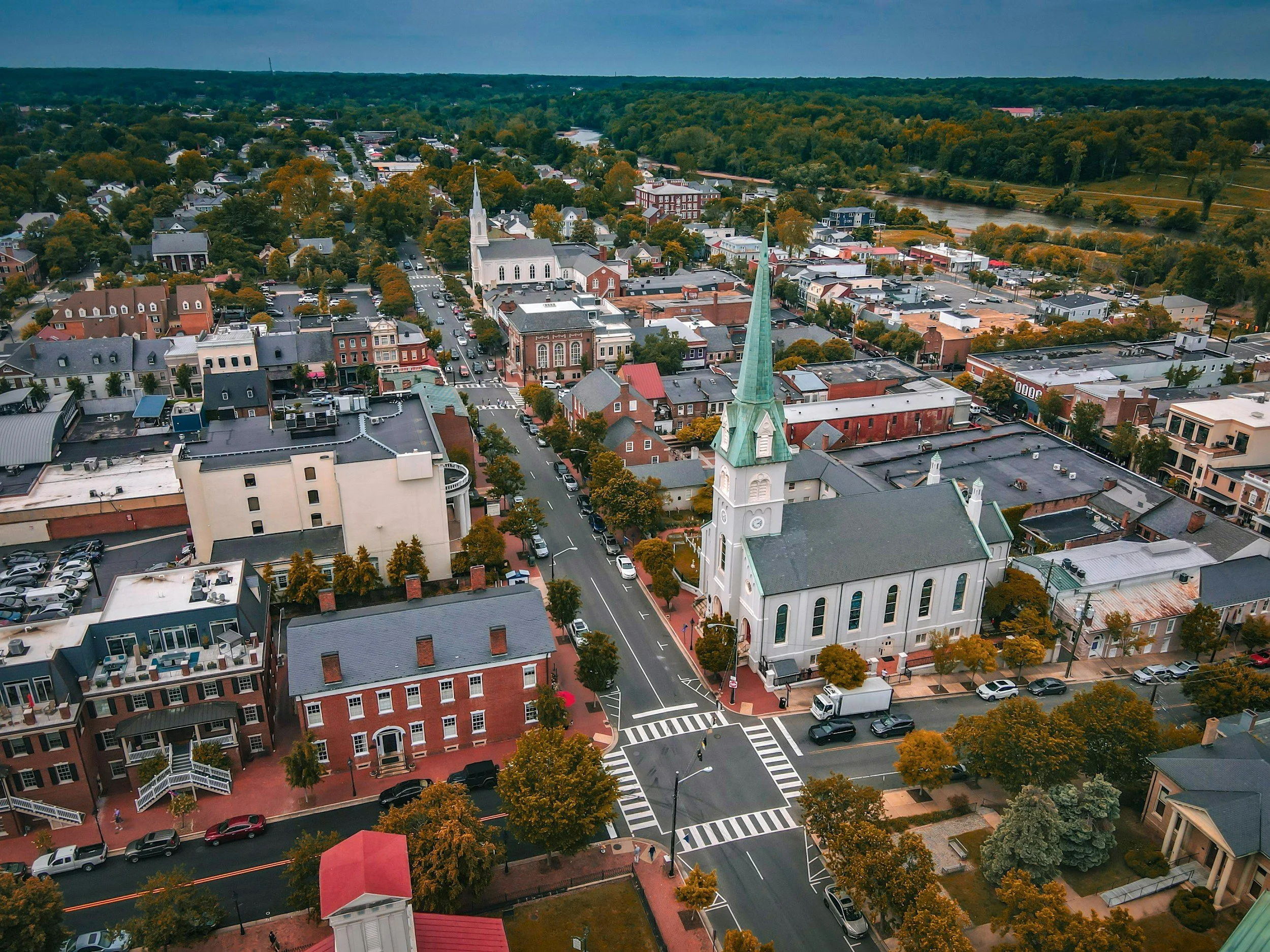 An aerial view of a downtown area with streets, trees, and a white church with a tall green steeple.