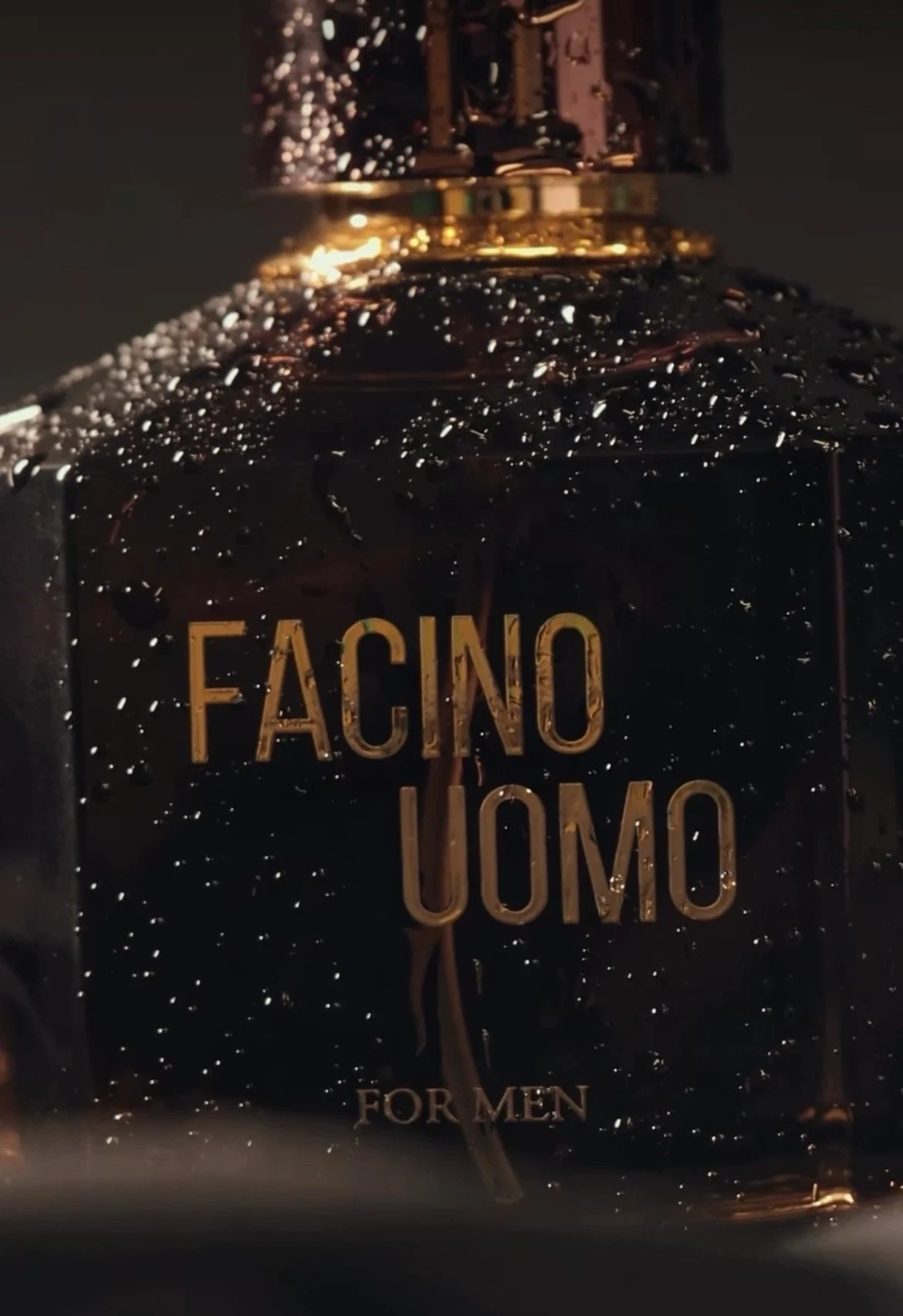 Close-up of a black perfume bottle with gold text that reads "FACINO UOMO" and smaller text "FOR MEN" at the bottom, covered in water droplets.