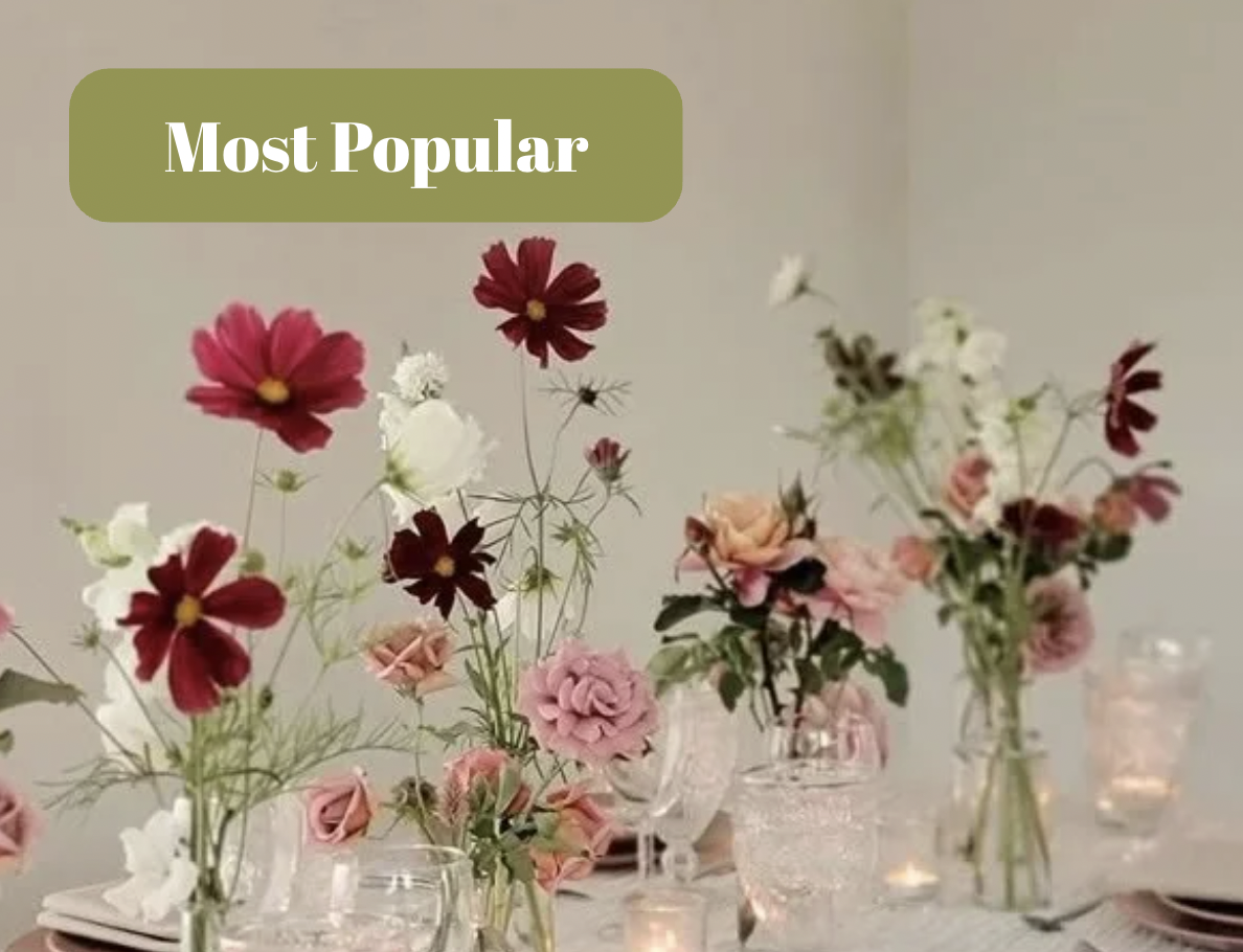 Elegant dining table decorated with pink and white flowers in glass vases, white napkins, pink plates, silverware, and lit candles.