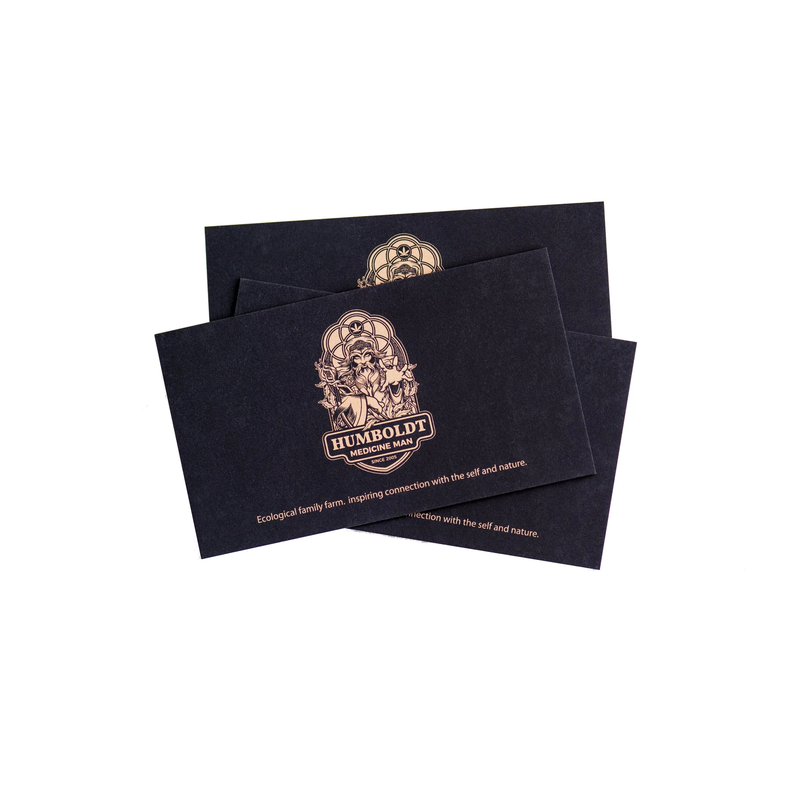 Black business cards with a gold logo of a bearded man holding a staff, labeled 'HUMBOLDT MEDICINE MAN,' with the tagline 'Ecological family farm, inspiring connection with the self and nature.'