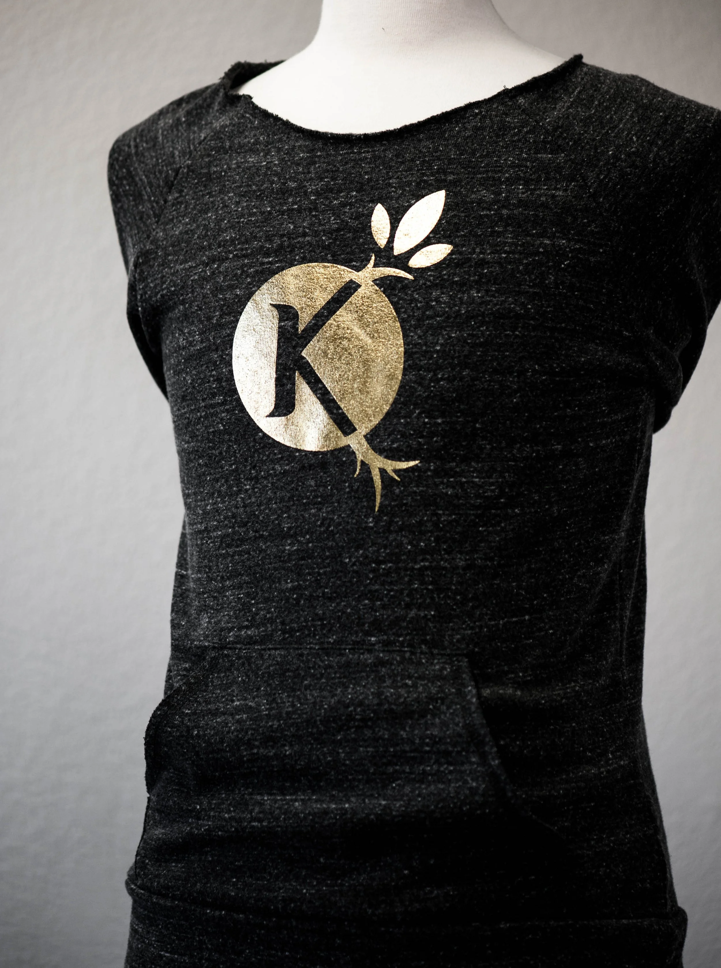 Black t-shirt with a gold logo featuring a lowercase 'k' inside a circle, with a branch and leaves. This was the original logo for Kiskanu Farms in Humboldt County