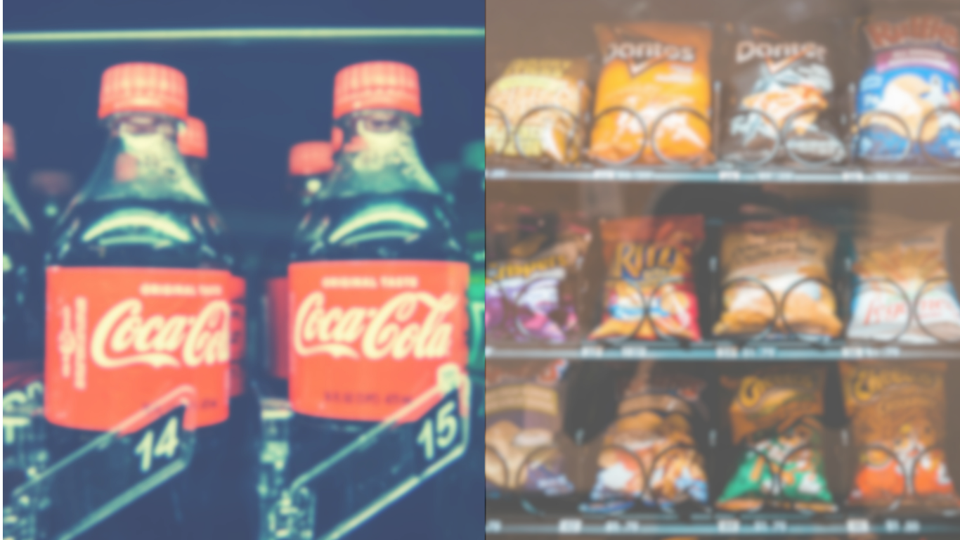 Blurry image of two Coca-Cola bottles on the left and an array of snack bags on the right in a store aisle.