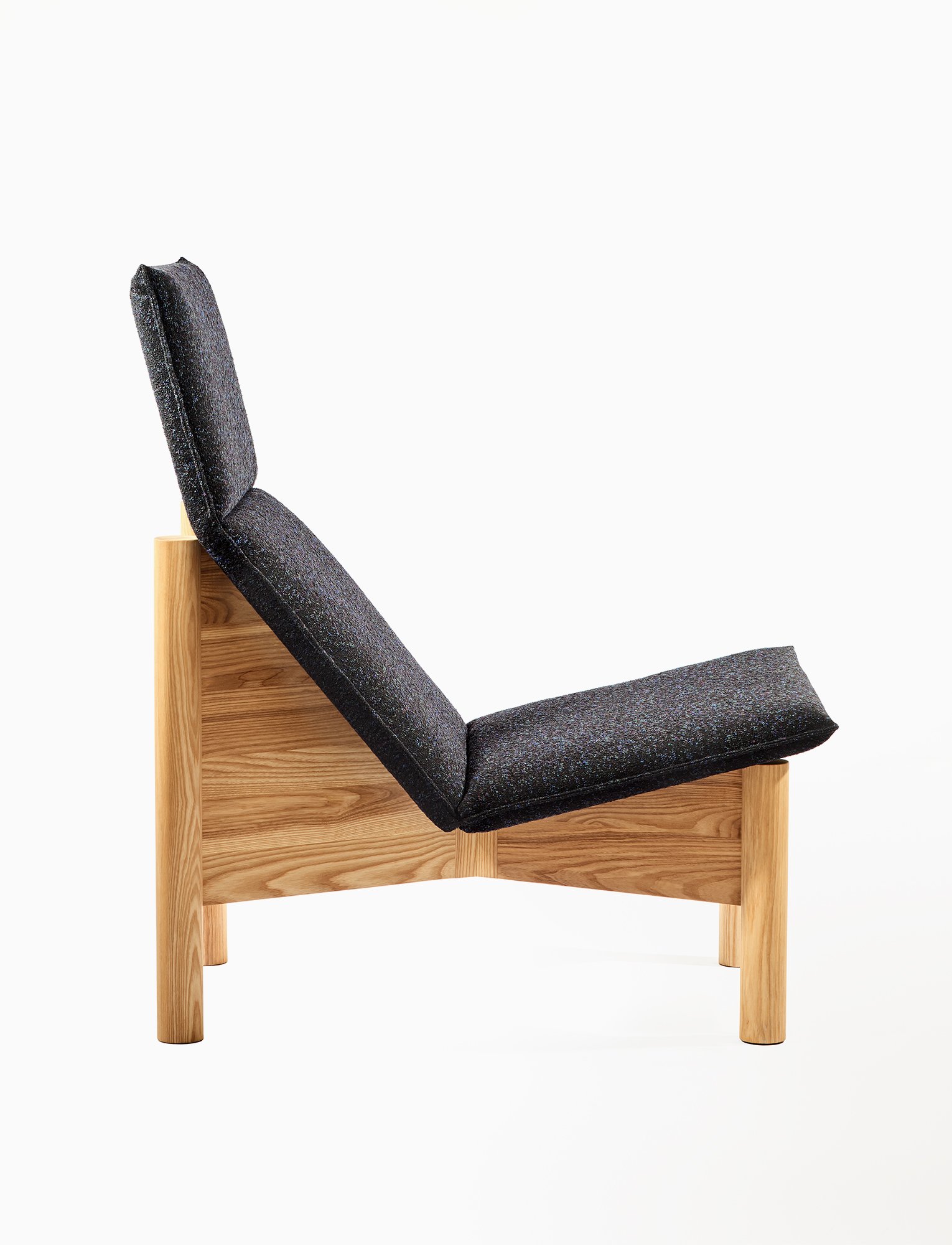 Side profile of the solid ash lounge chair showing its sculpted frame and upholstered seat.