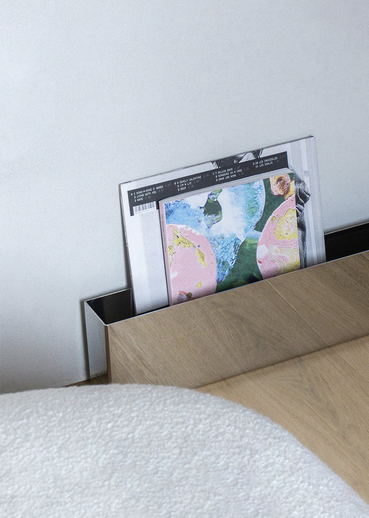 Mirror Shelf in polished stainless steel used to display magazines, showing its reflective surface and minimal wall-mounted profile.