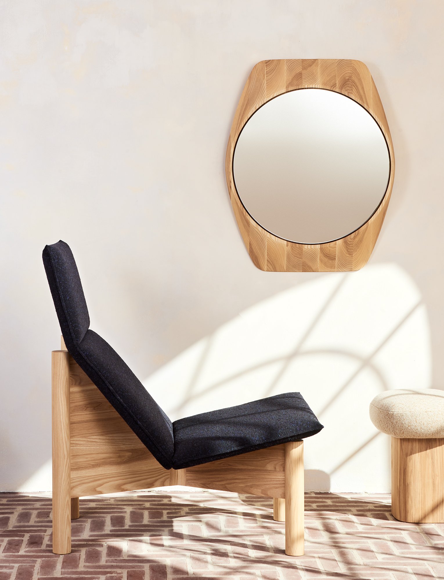 A solid ash lounge chair with a sculpted frame and upholstered seat, shown in a clean modern interior alongside the Tortue Mirror and Shuffle Stool.