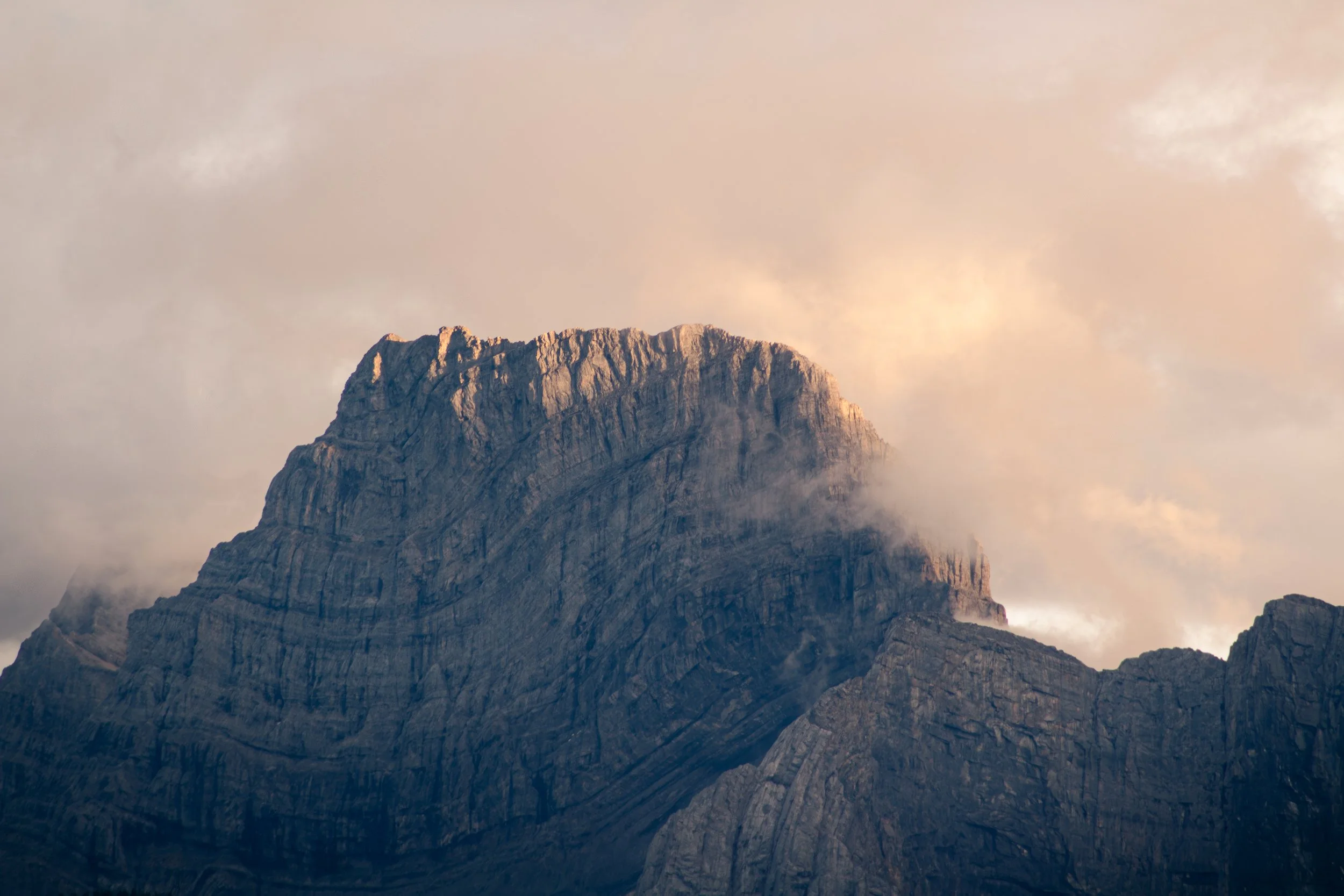 A rocky, jagged peak in Banff National Park,  backed by a thick fog and reflecting reddish sunlight. Taken in the Canadian Rockies