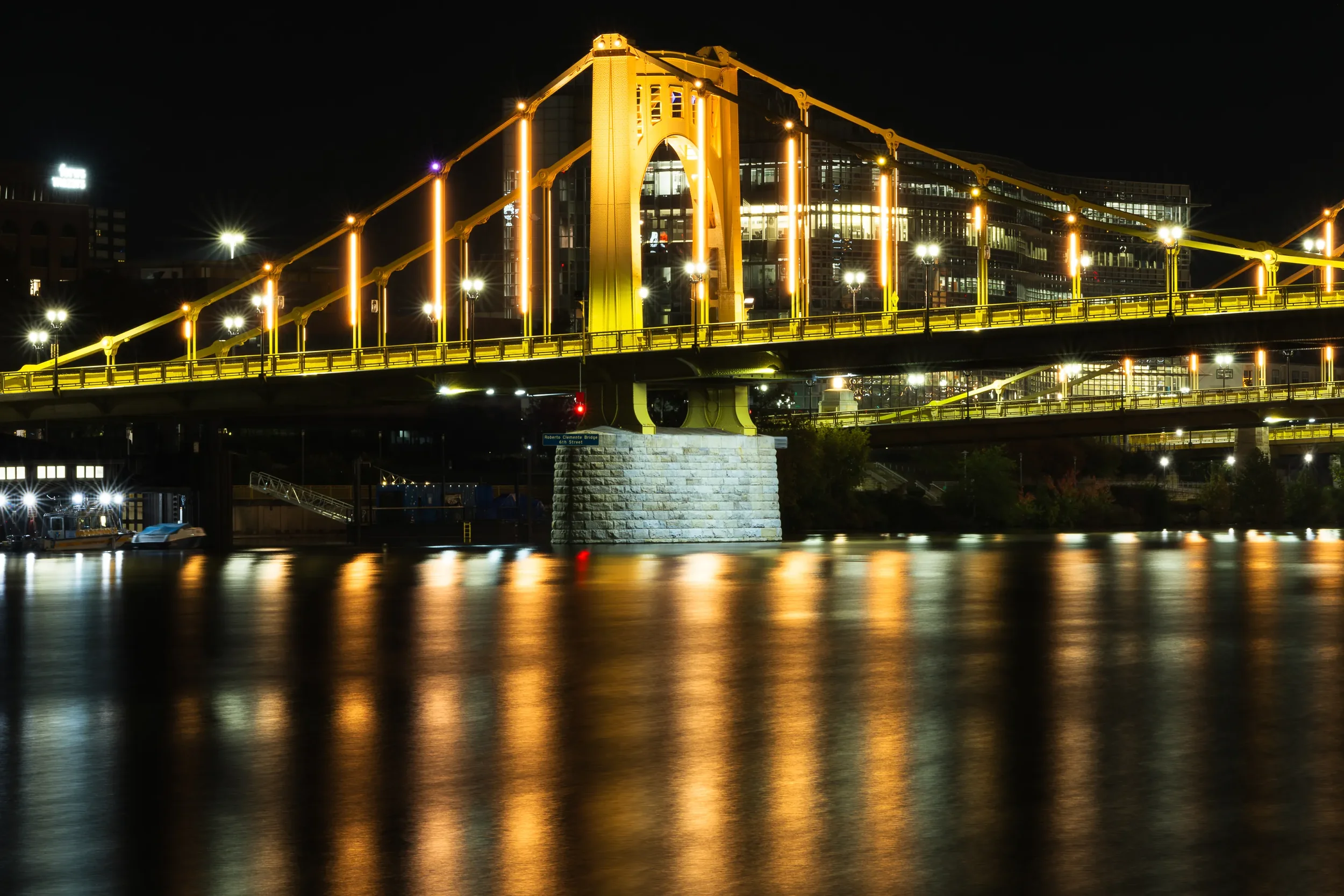 A golden bridge, the Roberto Clemente Bridge, over a river, which is reflecting the lights of the bridge in the water. In Pittsburgh, PA.