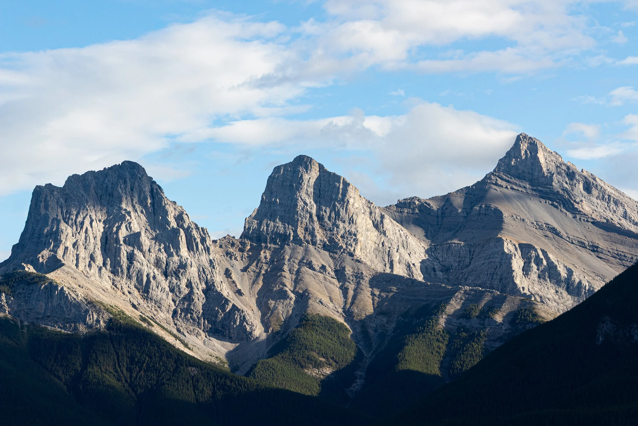 3 Mountain peaks, backed by a blue sky and white, cotton candy clouds at Banff National Park in the Canadian Rockies