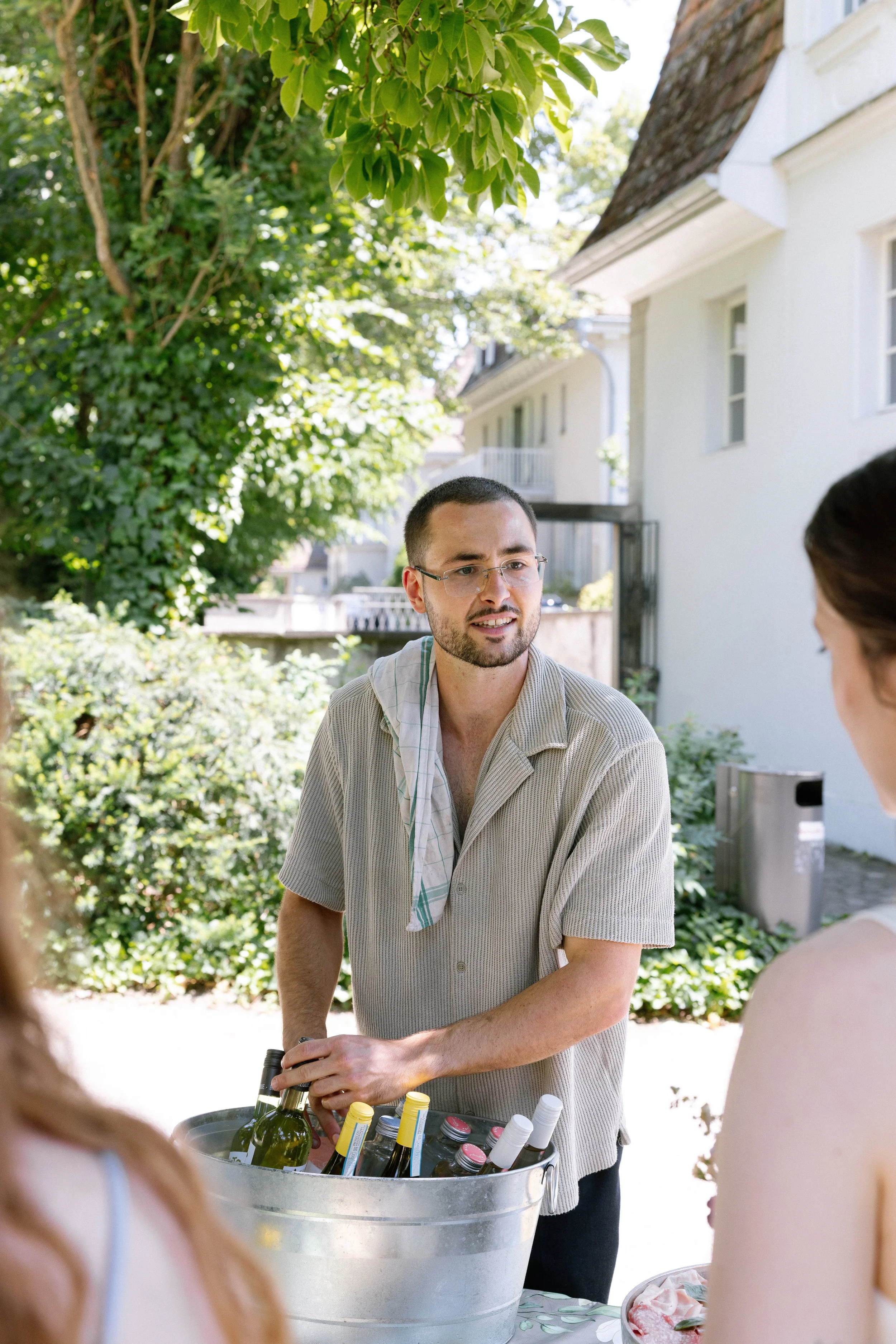 Mann serviert Wein bei einer Outdoor-Party im Garten, umgeben von Frauen.
