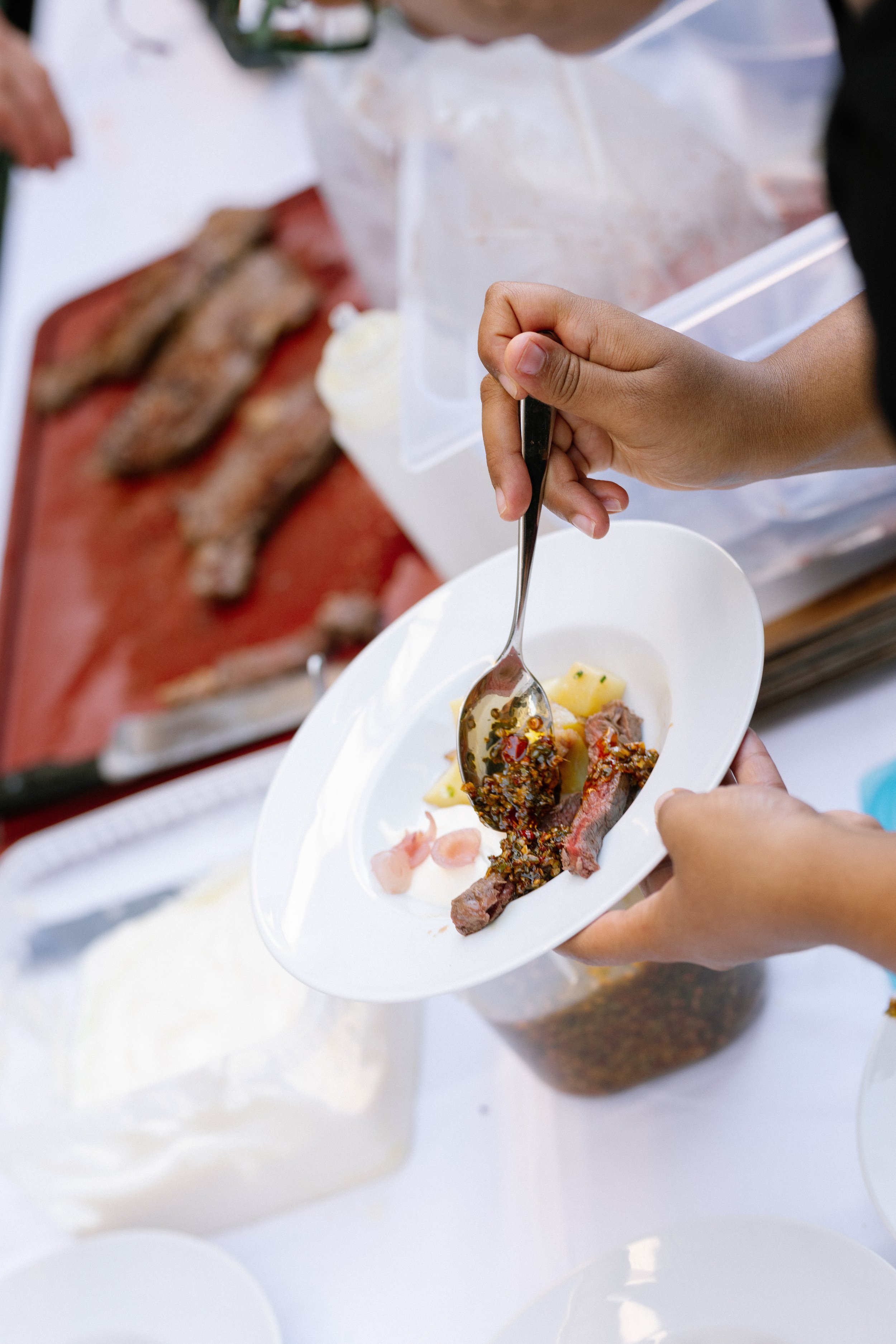Eine Person serviert Rindfleisch mit Chilisoße auf einem weißen Teller.
