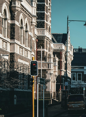 Street scene with ornate historic buildings, a traffic light showing red, and a parked car under a clear blue sky.
