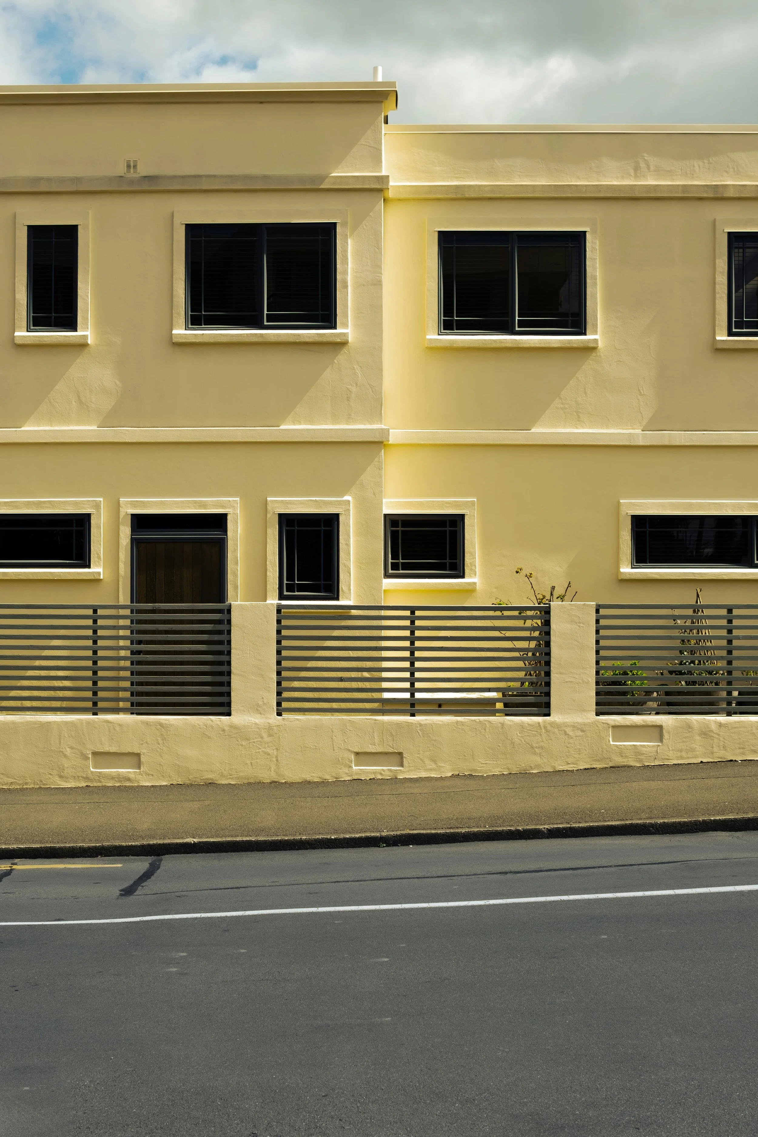 Yellow multi-story building with black-framed windows and a horizontal metal fence along the sidewalk.