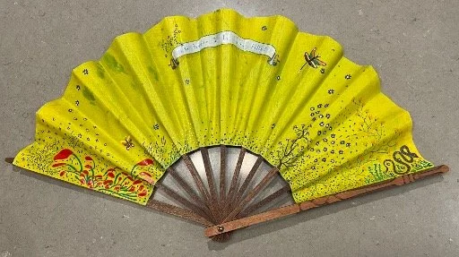 A yellow folding hand fan with decorative patterns and designs.