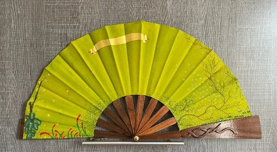 Handheld folding fan with a green leaf design and a wooden handle.