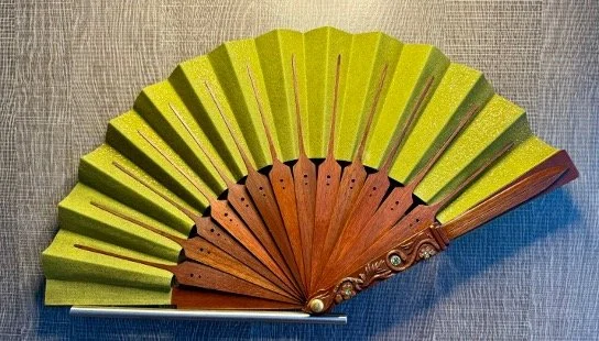 A decorative handheld fan with light green and brown segments, displayed closed.