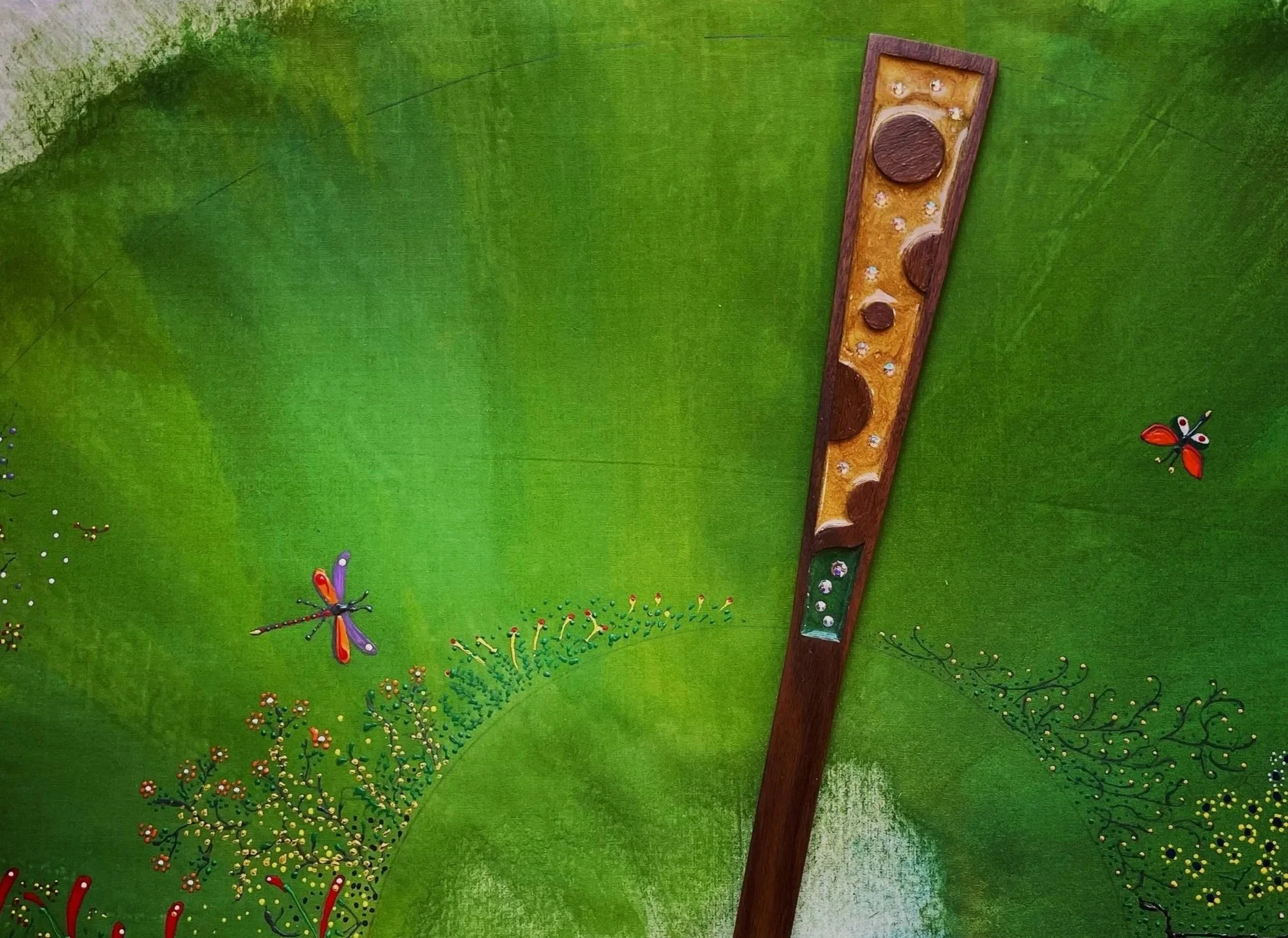 Close-up of a green painted surface with detailed butterfly and flower designs, featuring a wooden fan guard with various ornaments including crystals inside.