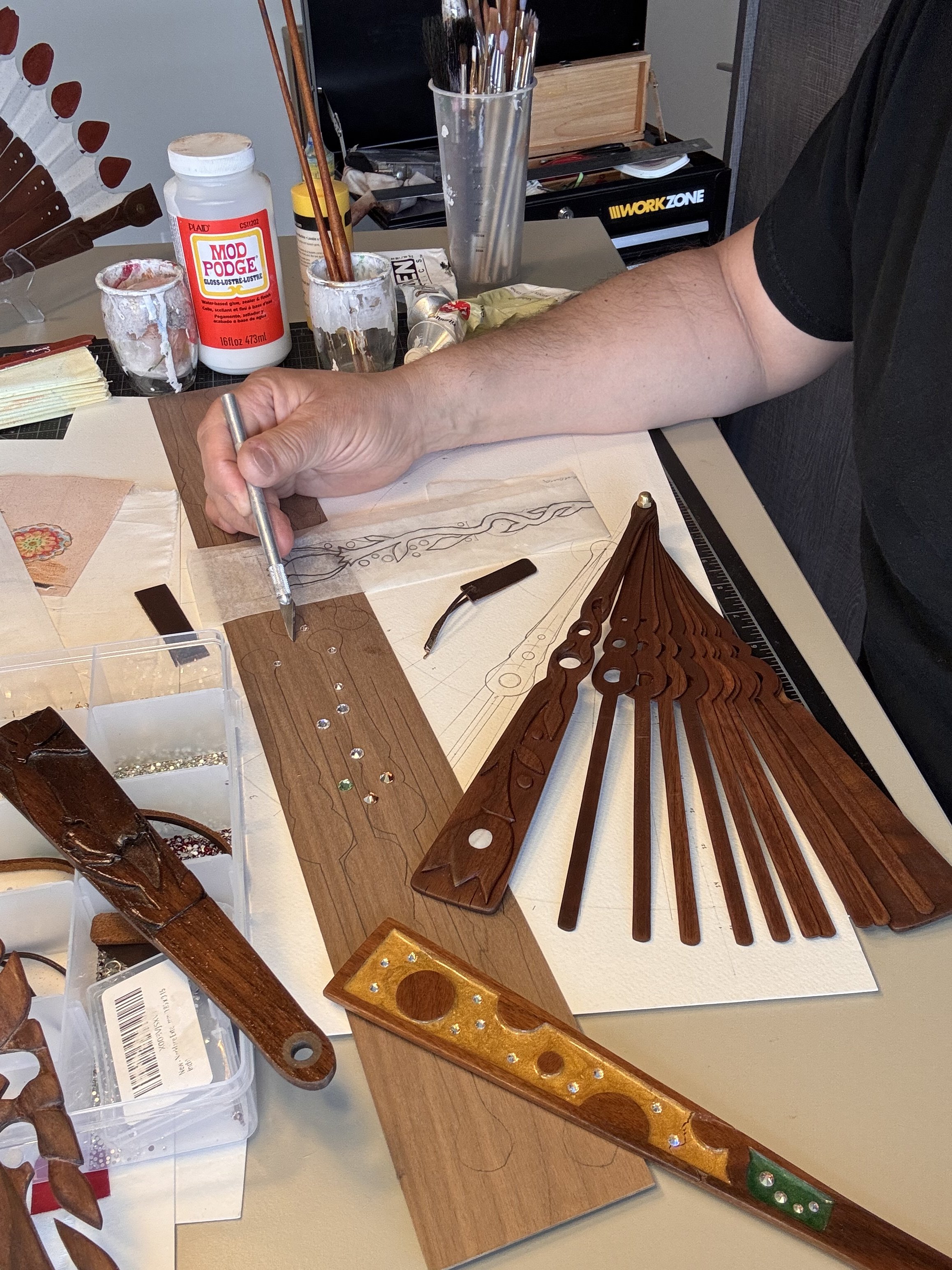 A person working on a fan making project at a workspace with wooden parts, tools, and paint supplies.