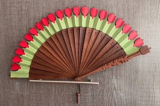 Decorative hand fan with green, brown, and red accents on a textured surface.