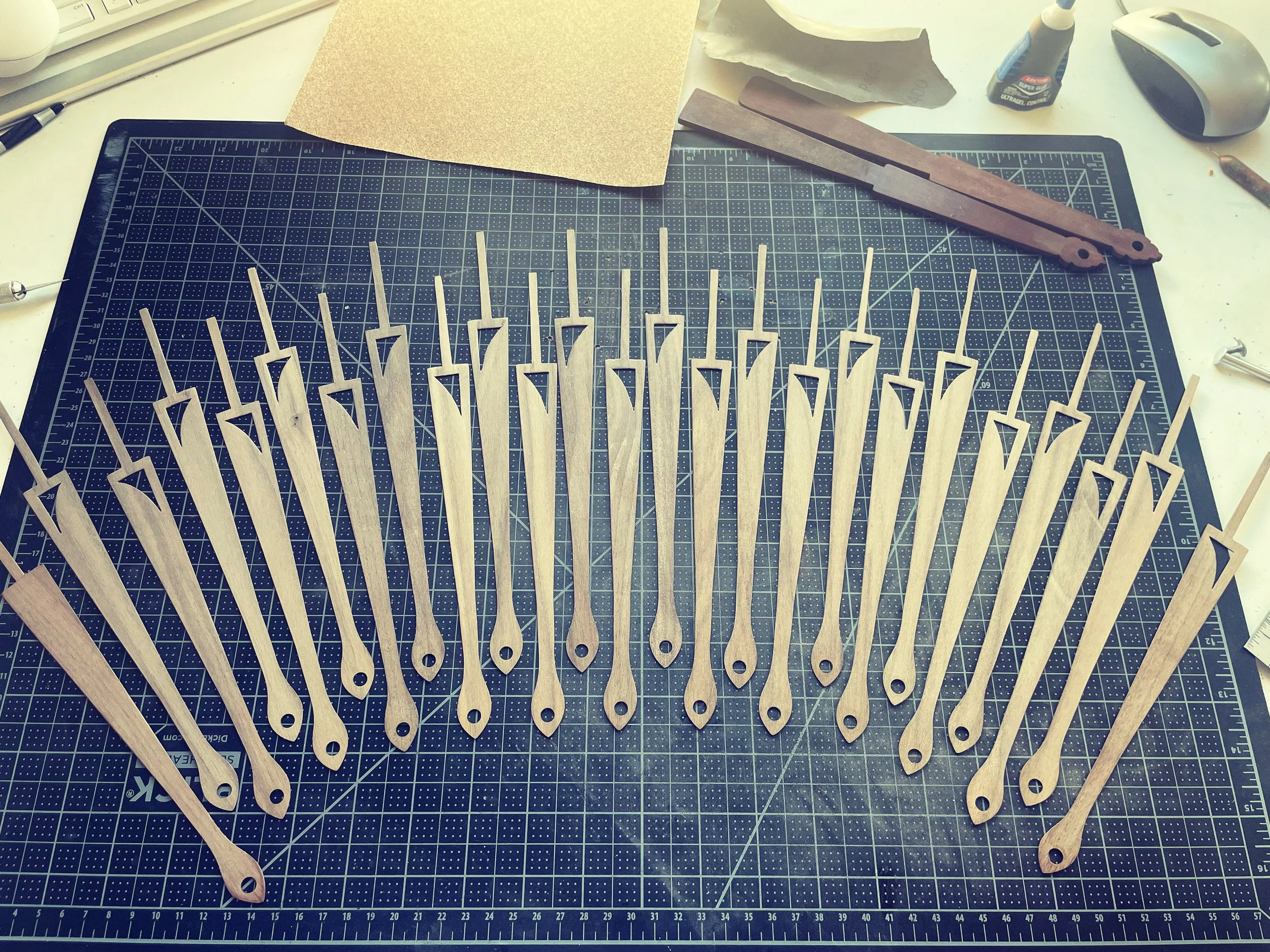 Multiple small wooden fan staves arranged on a cutting mat, with some tools and materials in the background.