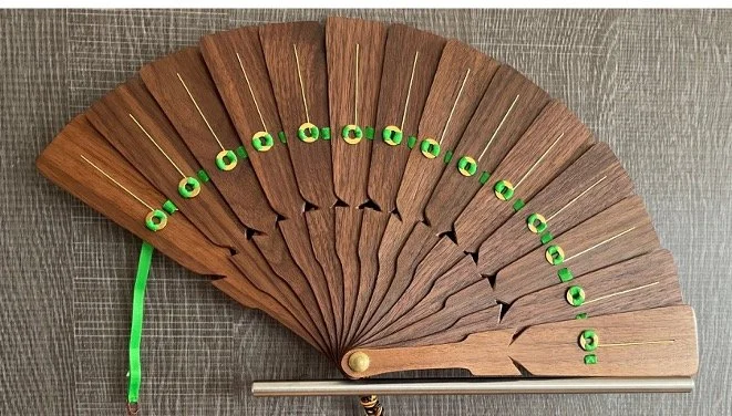 A closed decorative folding fan made of wood with green ribbon attached to the top edge.