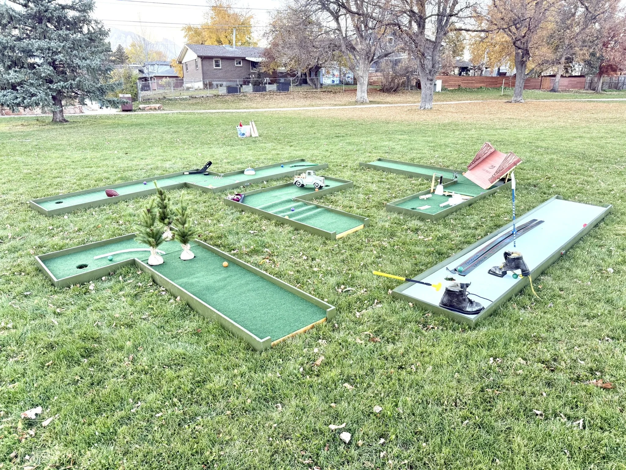 Portable mini golf set up with multiple holes and themes including Red Rocks Amphitheater, skiing, Colorado sports teams, autumn vintage farm truck, and fall pumpkins. For rent.