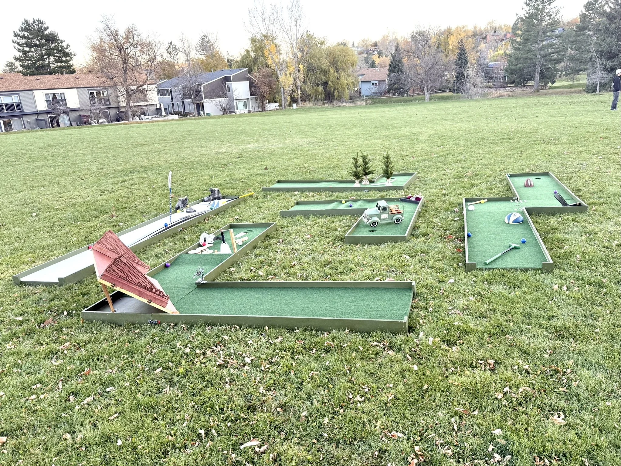 Portable mini golf set up with multiple holes and themes including Red Rocks Amphitheater, skiing, Colorado sports teams, autumn vintage farm truck, and fall pumpkins. For rent.