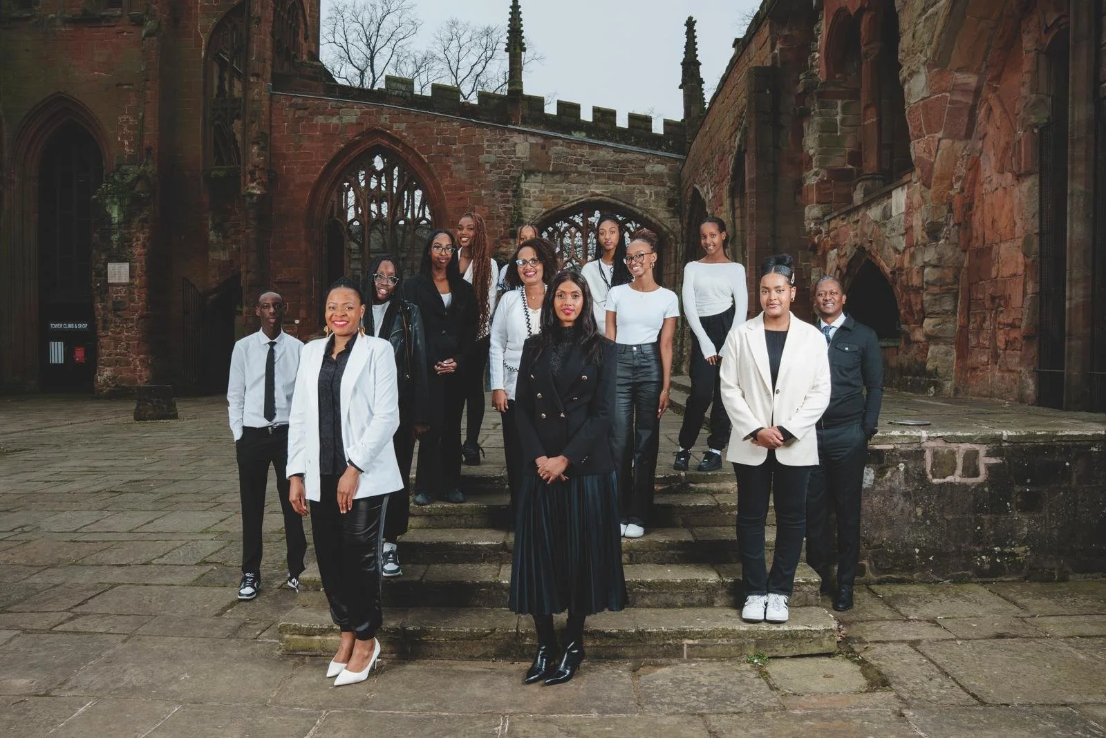 Group of 14 diverse professionals posing outdoors in front of an old brick building with gothic architecture.